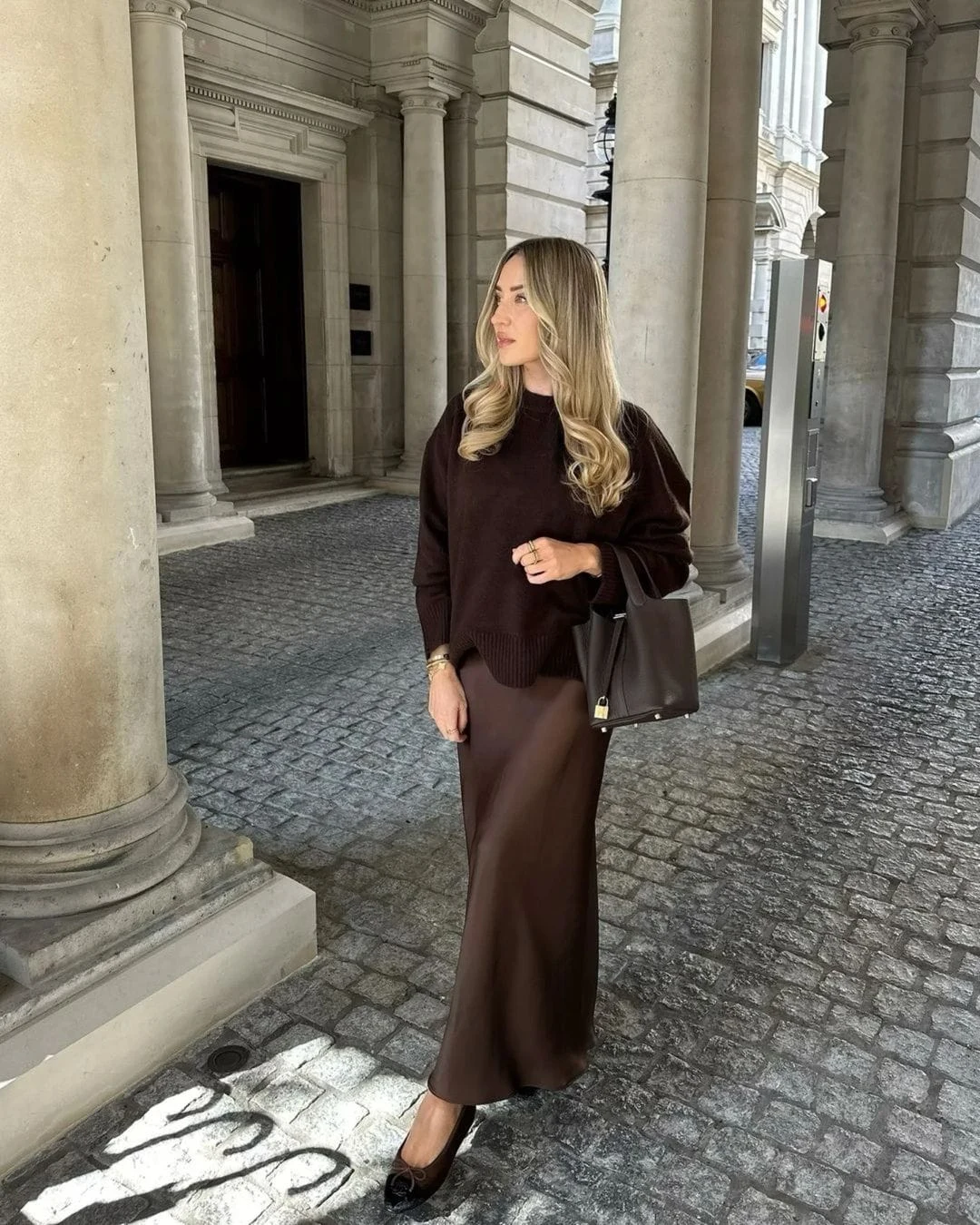This outfit combines a chocolate-brown sweater with a sleek maxi skirt for a polished, monochromatic look. Paired with black ballet flats and a structured brown bag, it’s a refined yet understated choice for cold-weather sophistication.