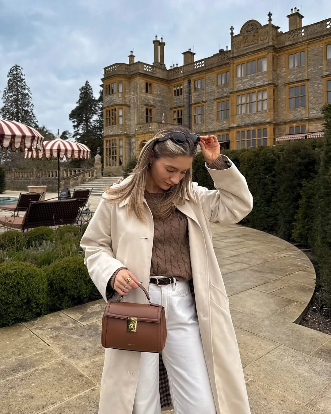 Cream trench coat over a chunky chocolate cable-knit sweater with crisp white jeans underneath.
