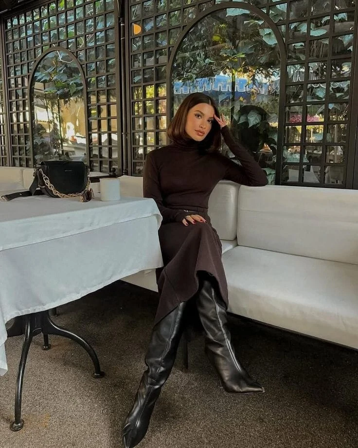 Fitted espresso turtleneck sweater dress paired with pointed knee-high black boots and a chain-handle bag.