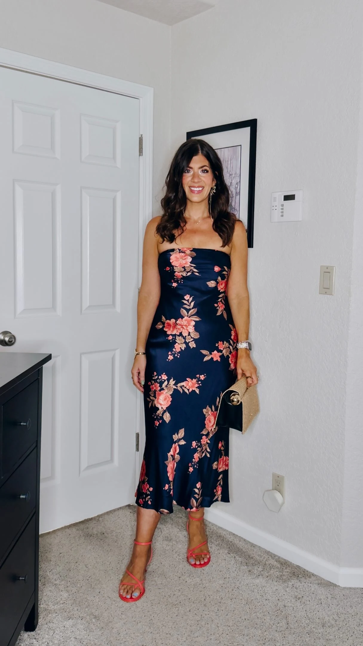 Woman in a strapless navy floral midi dress with a flared hem and coral-red strappy sandals.