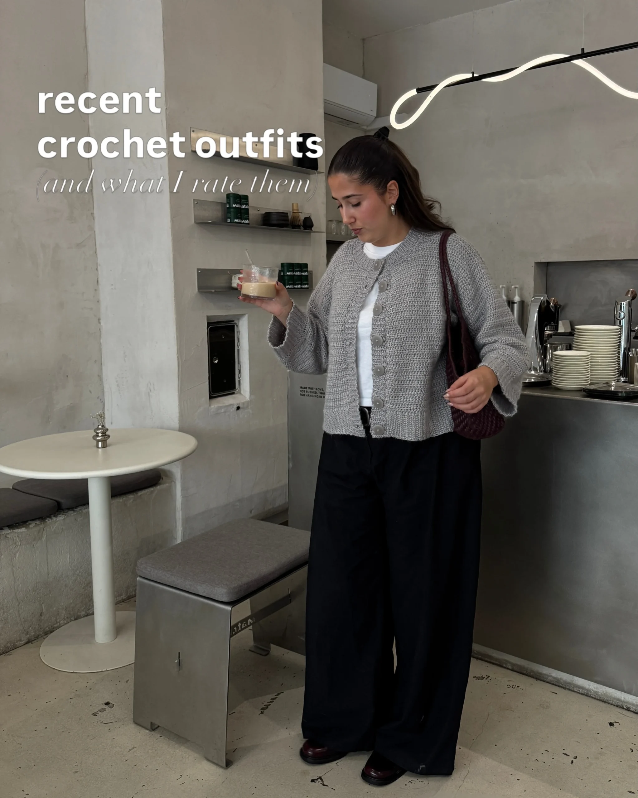Chunky gray buttoned cardigan over a white top, black wide-leg trousers, and a burgundy shoulder bag.