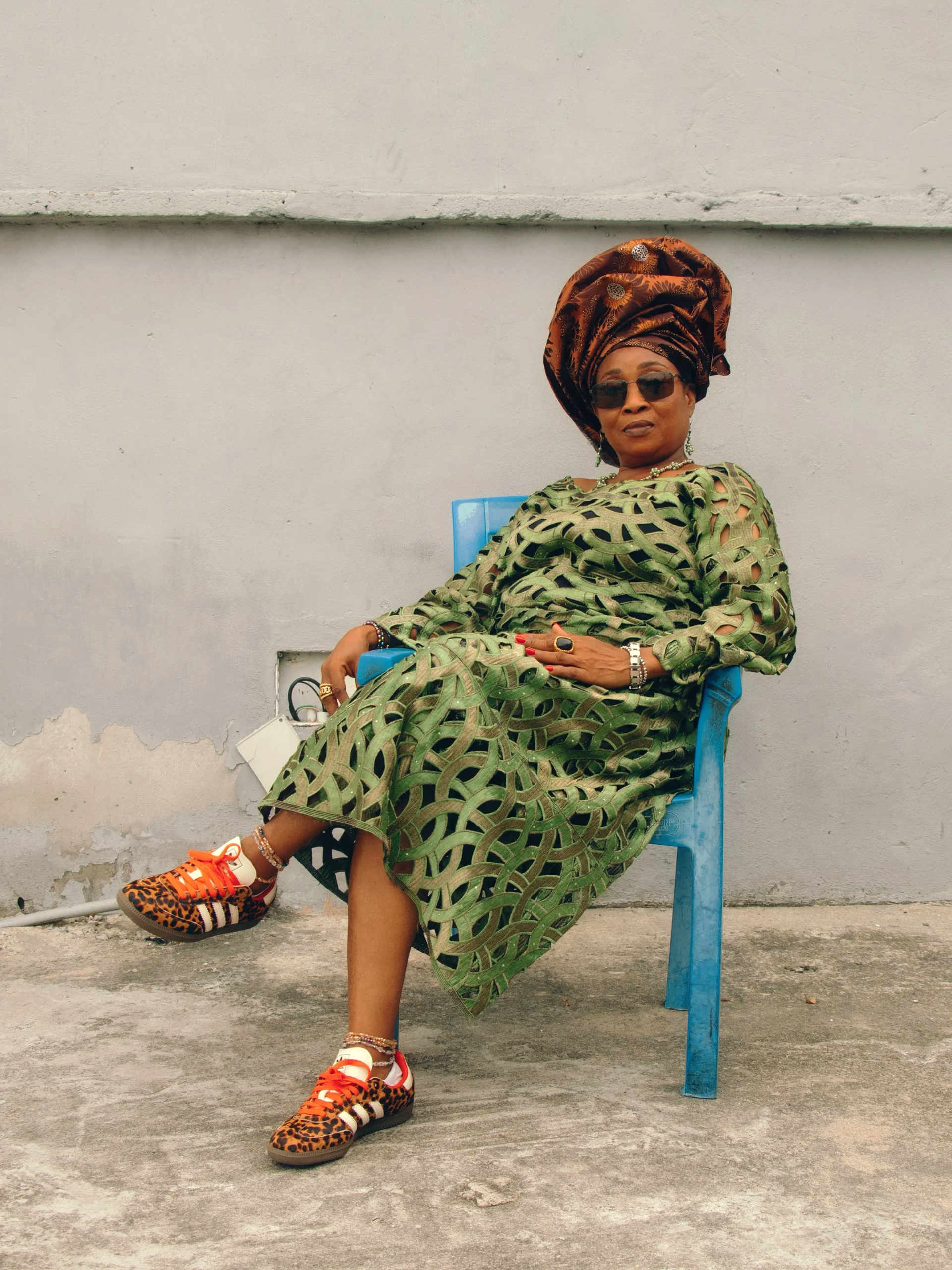 Green geometric midi dress and gele headwrap styled with leopard-print Adidas Sambas and gold jewelry.