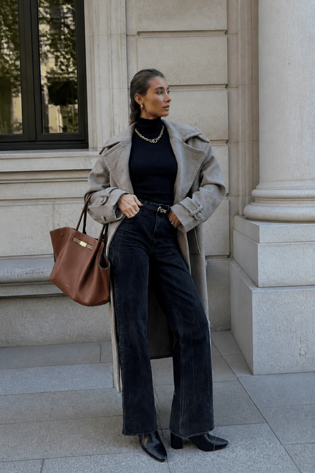 Woman in a long taupe trench coat, black wide-leg jeans, and sleek black ankle boots.