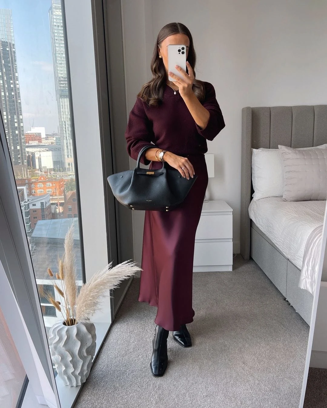 This outfit combines a silky maroon maxi skirt with a matching sweater, creating a sleek monochrome look. Paired with black leather boots and an elegant structured bag, it’s perfect for a chic winter day.