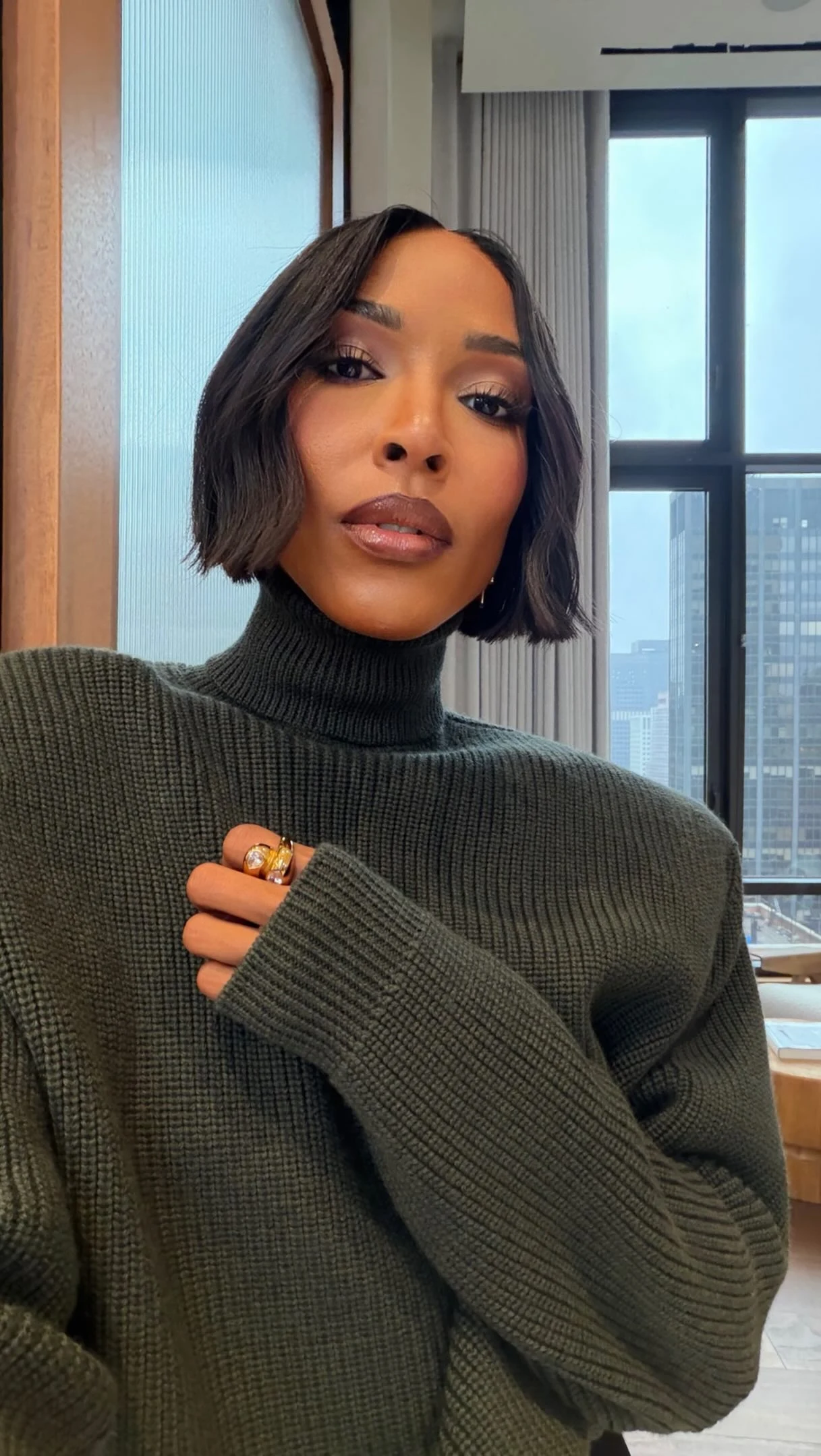 Oversized olive ribbed turtleneck with structured shoulders worn with black leggings and pointed-toe heels.