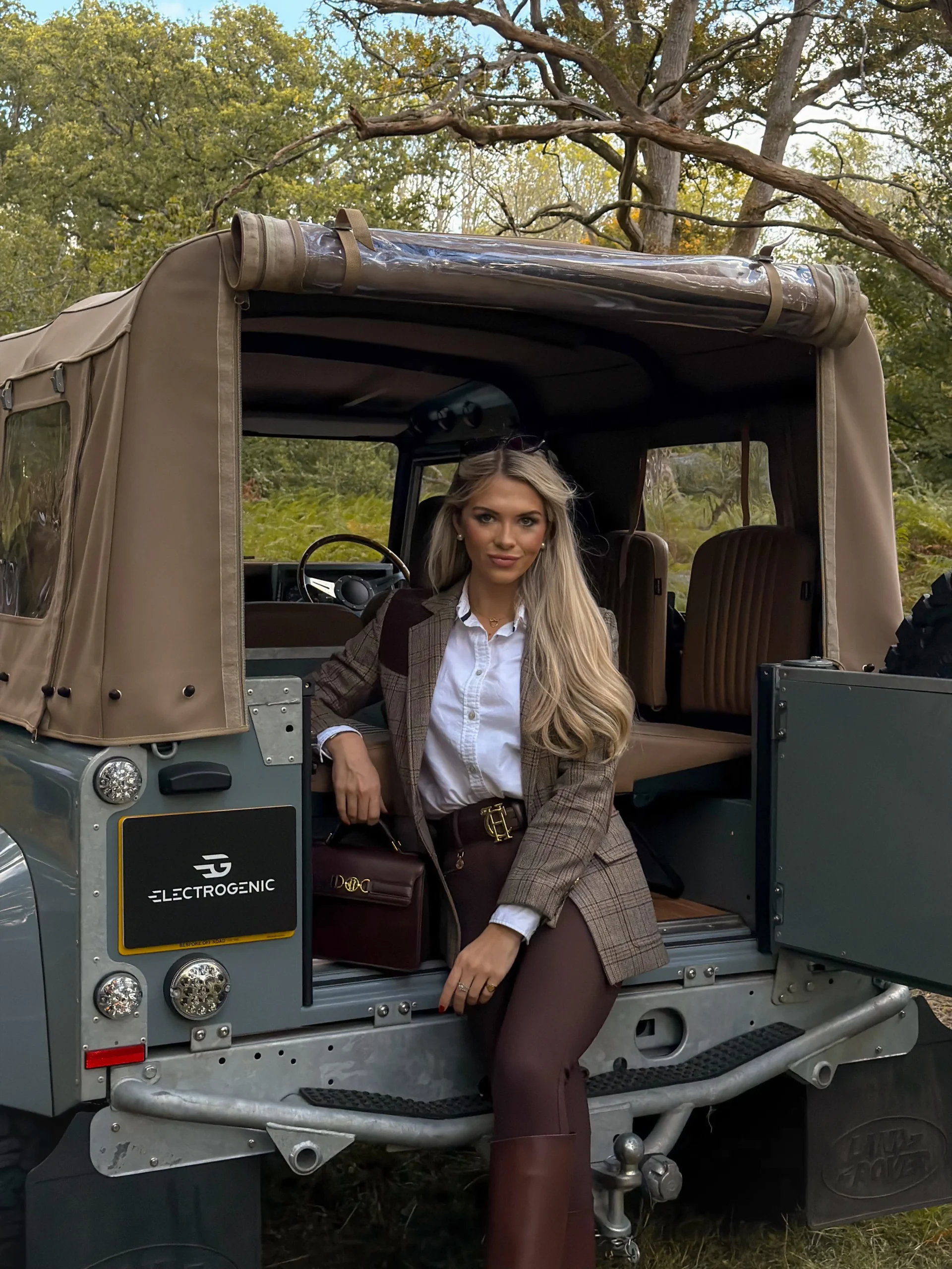 Brown plaid blazer over a white shirt and dark trousers with tall brown boots and a burgundy handbag.