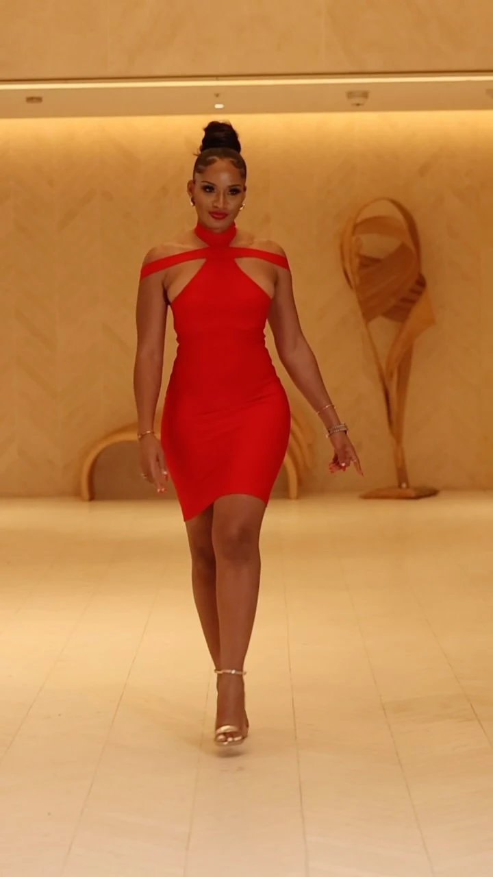 Woman wearing a red halter mini dress with shoulder cutouts and gold strappy heels.