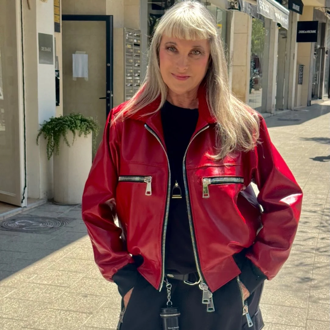 Bright red leather bomber jacket with silver zippers worn over all-black top and pants, hands in pockets.