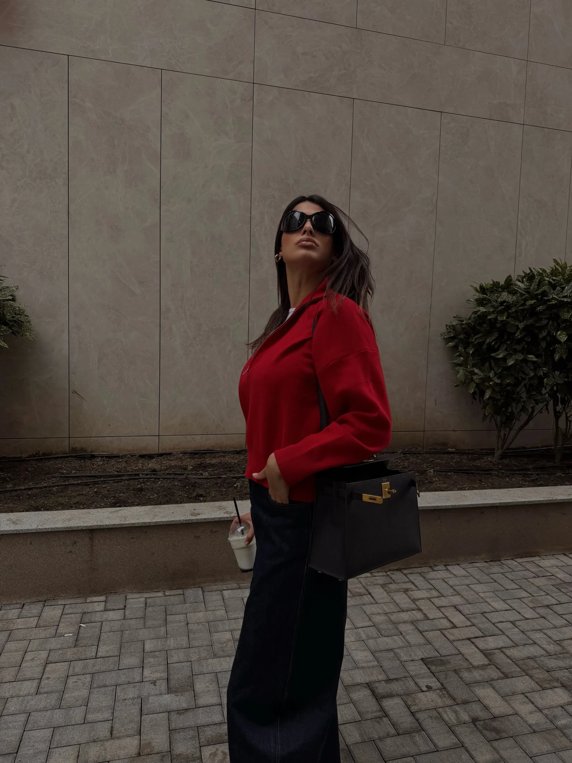 Relaxed red sweater with dark wide-leg jeans, black sunglasses, and a structured black handbag with gold clasp.