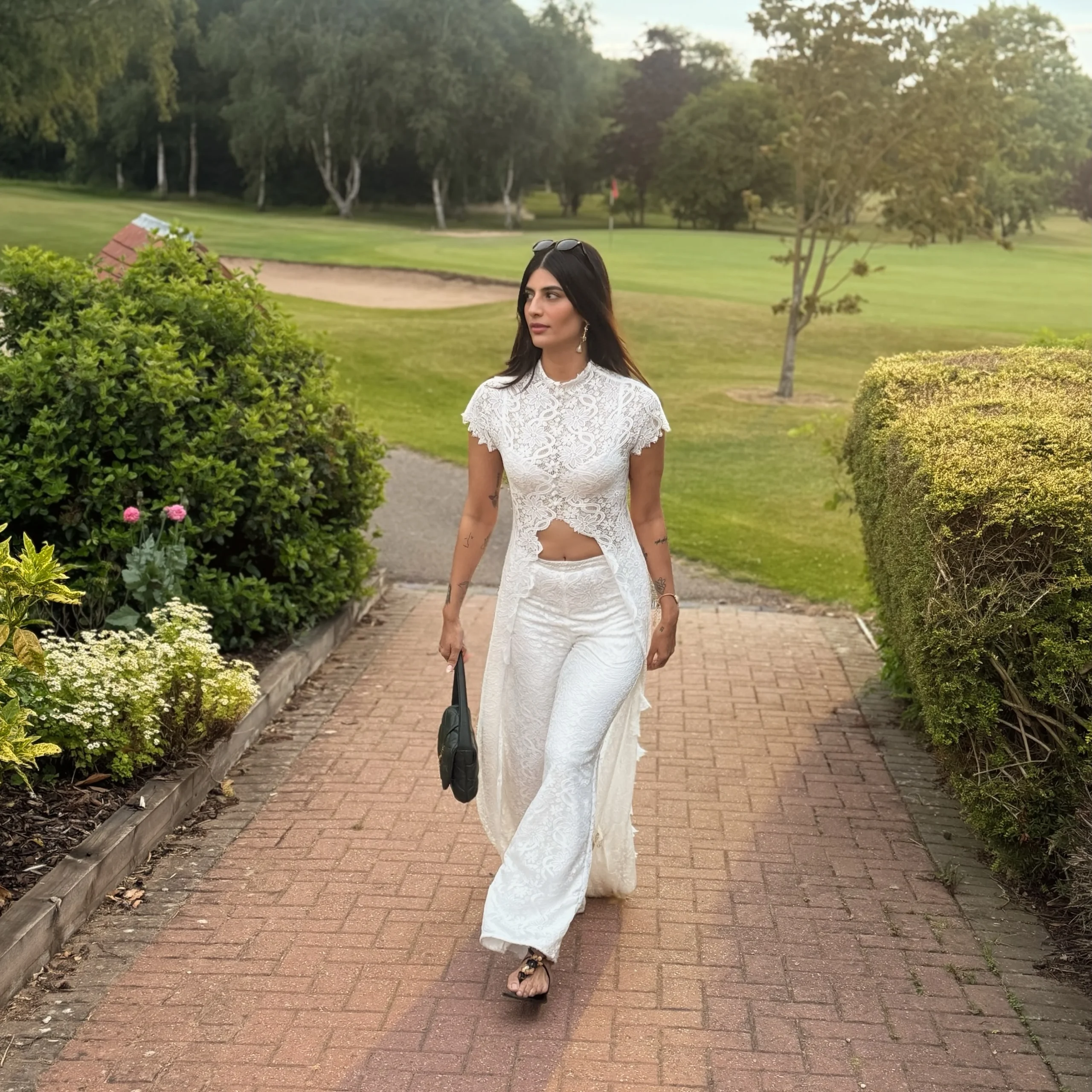 White lace high-neck crop top and wide-leg pants with sheer side panels on a brick path.