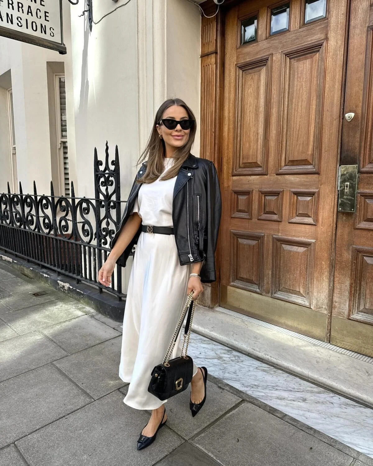 White satin skirt and tee styled under a black leather jacket with slingback flats and handbag.