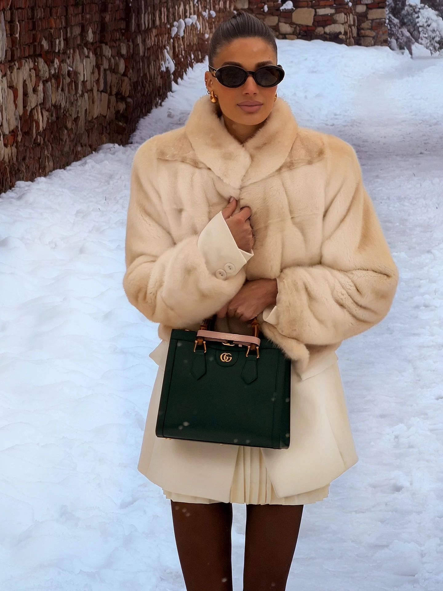 Woman wearing a voluminous beige faux-fur coat, black turtleneck, wide-leg jeans, and black gloves.