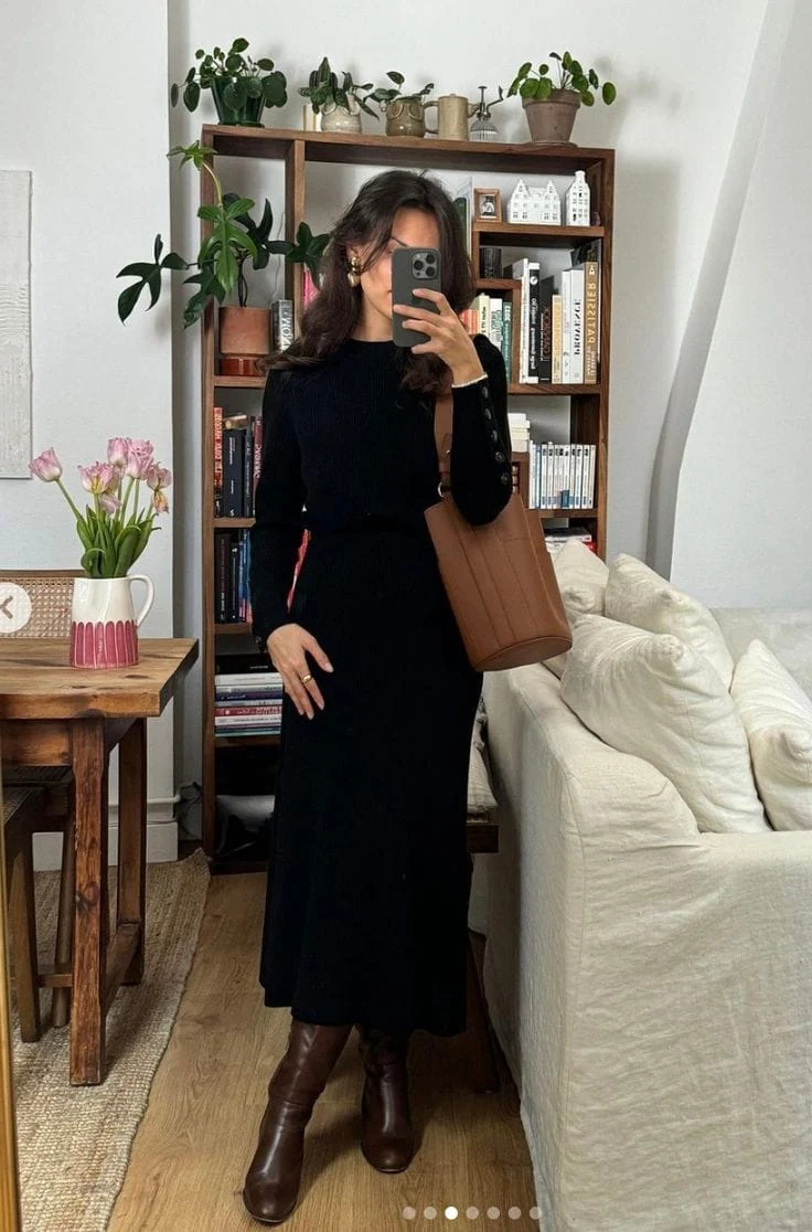 A classic black knit sweater dress is effortlessly elevated by mid-heel brown leather boots for a refined, everyday look. The structured tan tote and gold statement earrings add dimension—style with soft waves and a bold ring for a hint of modern sophistication.