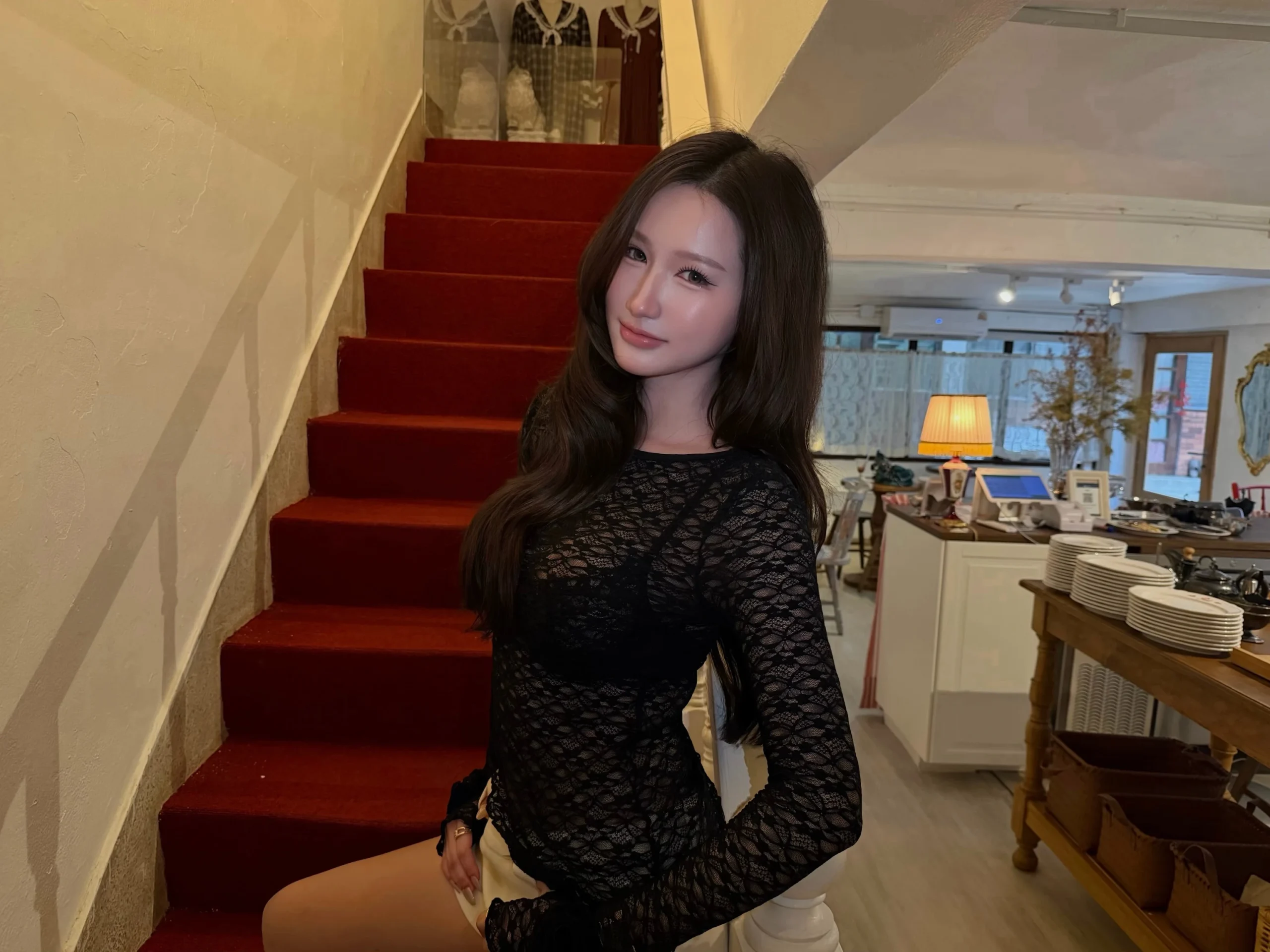 Woman in a black sheer lace long-sleeve top styled with light-colored trousers.