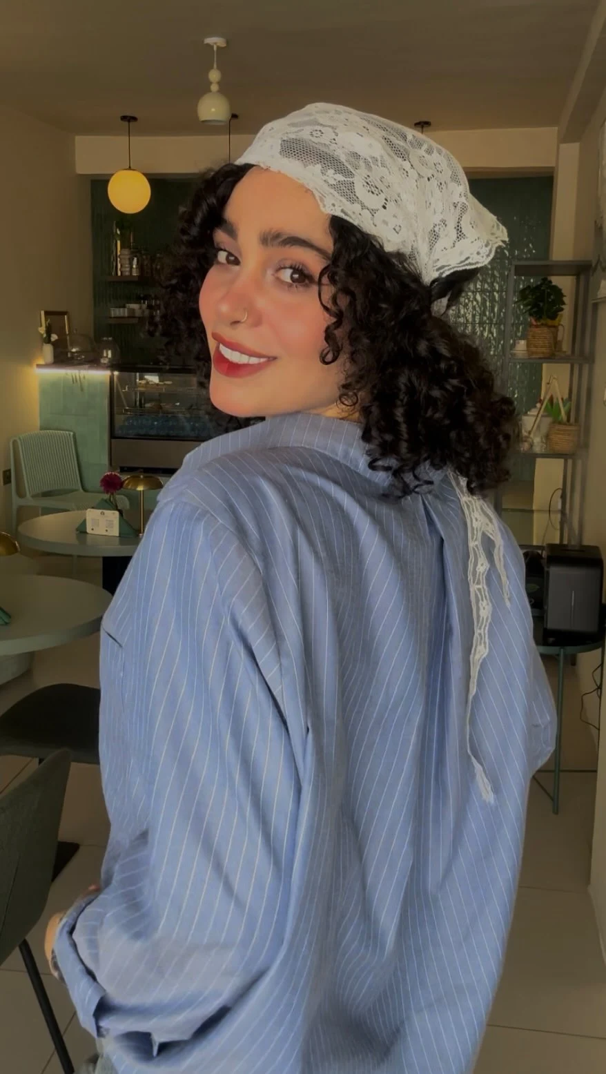 Loose blue pinstriped shirt worn with a white lace headscarf draped down the back.