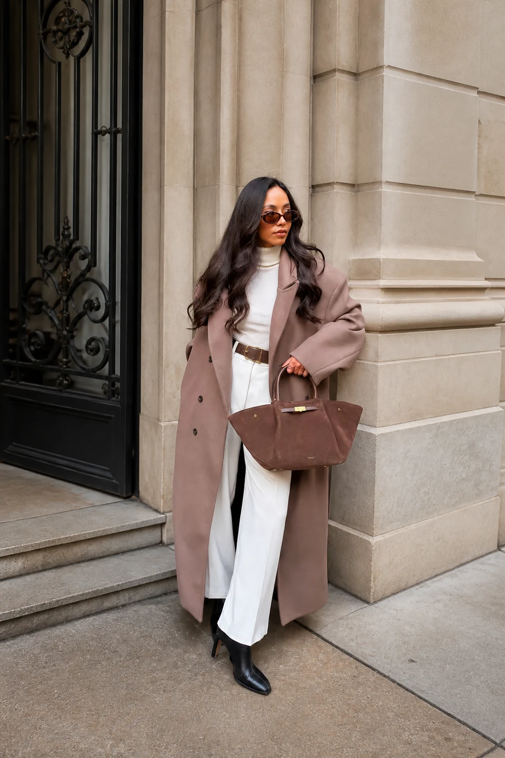 Woman in blush wool coat, white turtleneck, wide trousers, and black ankle boots outdoors.