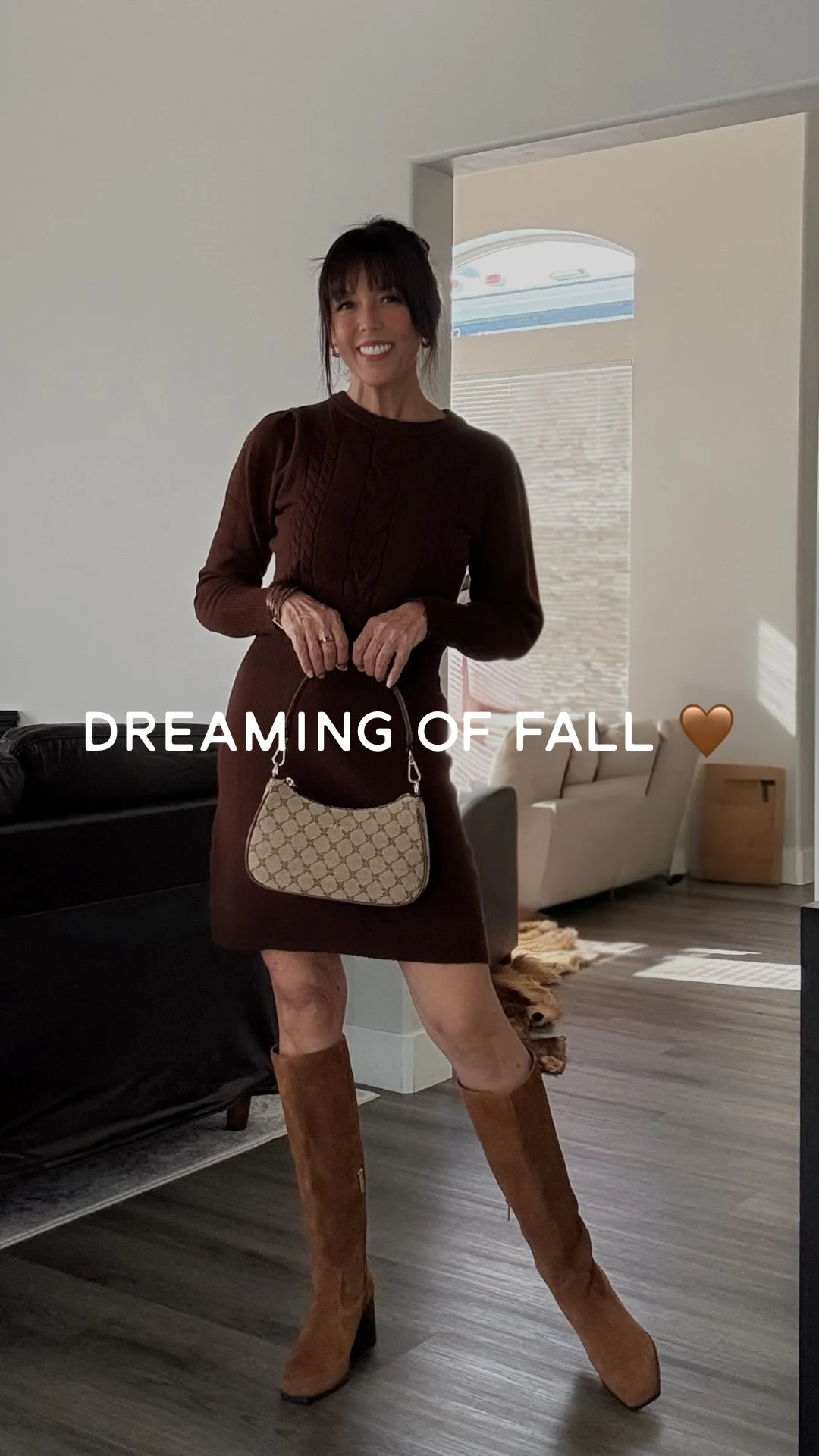 Woman wearing a brown cable-knit sweater dress, tan knee-high boots, and a small patterned shoulder bag.