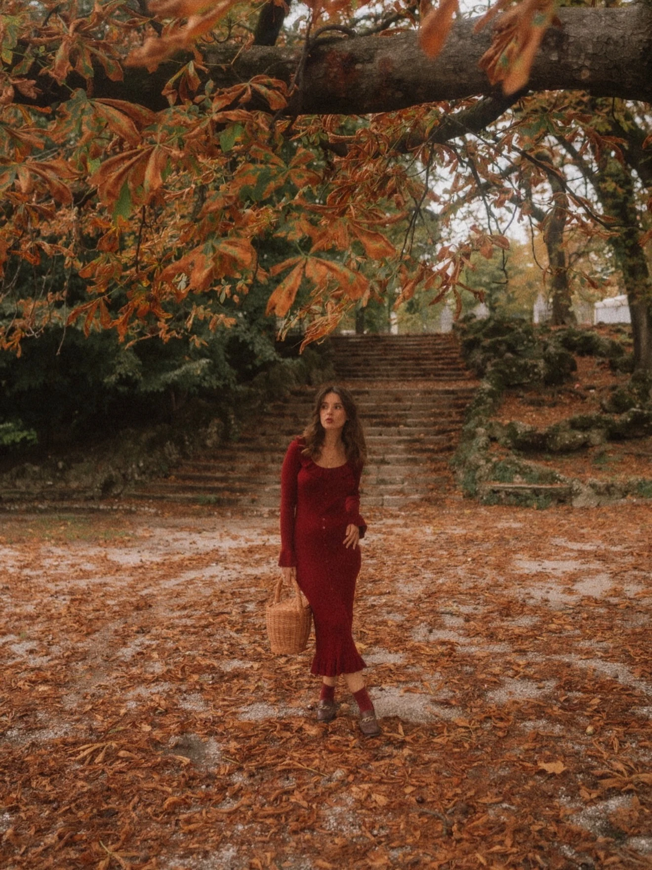 Woman in a fitted burgundy long sleeve midi dress carrying a tan woven basket bag.