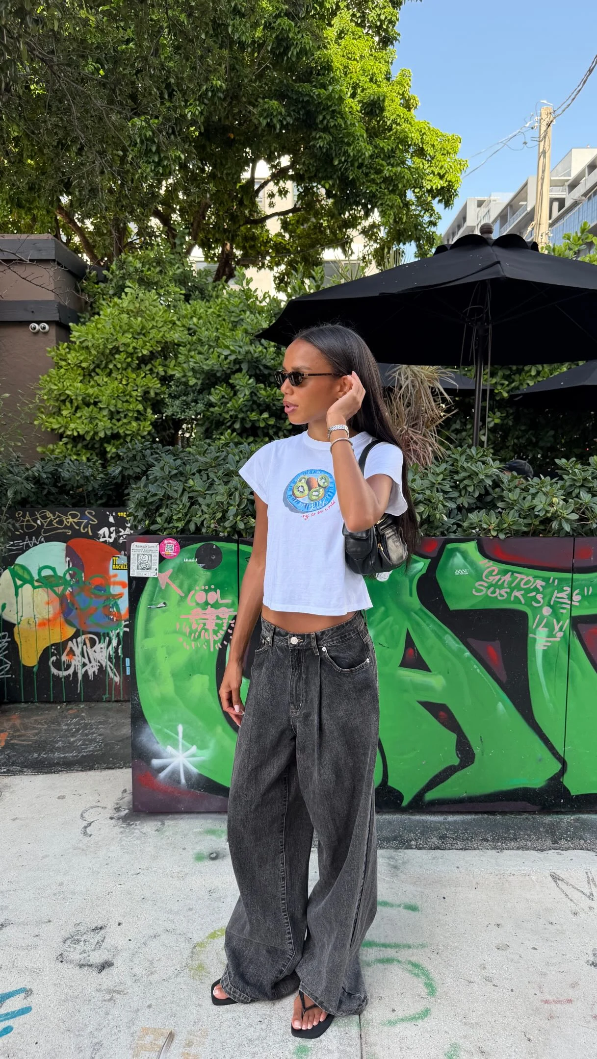 Woman wearing extremely baggy dark denim jeans, white cropped tee, and black flip-flops.
