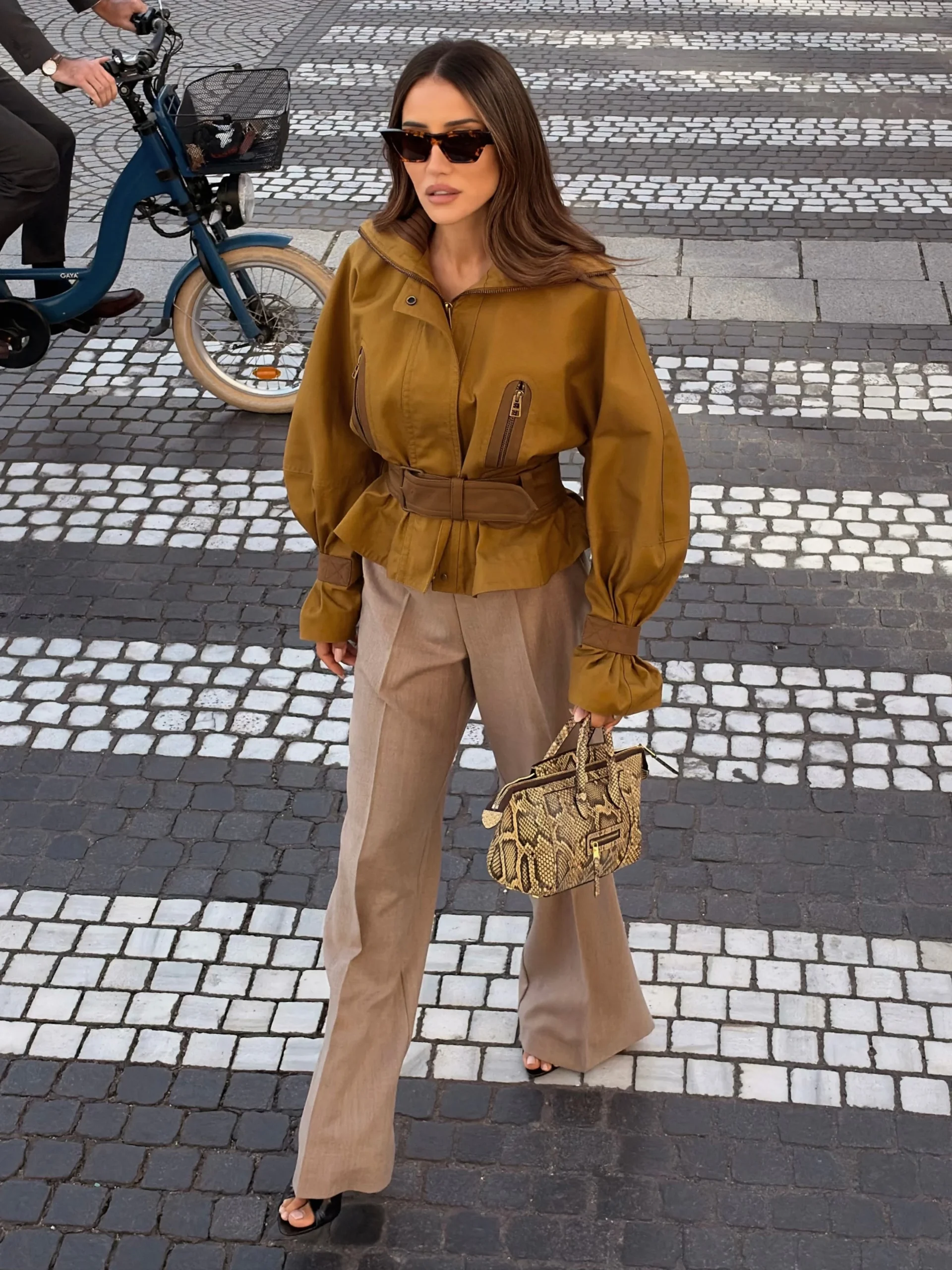 Mustard belted jacket with voluminous sleeves paired with light taupe wide-leg trousers and dark open-toe shoes.