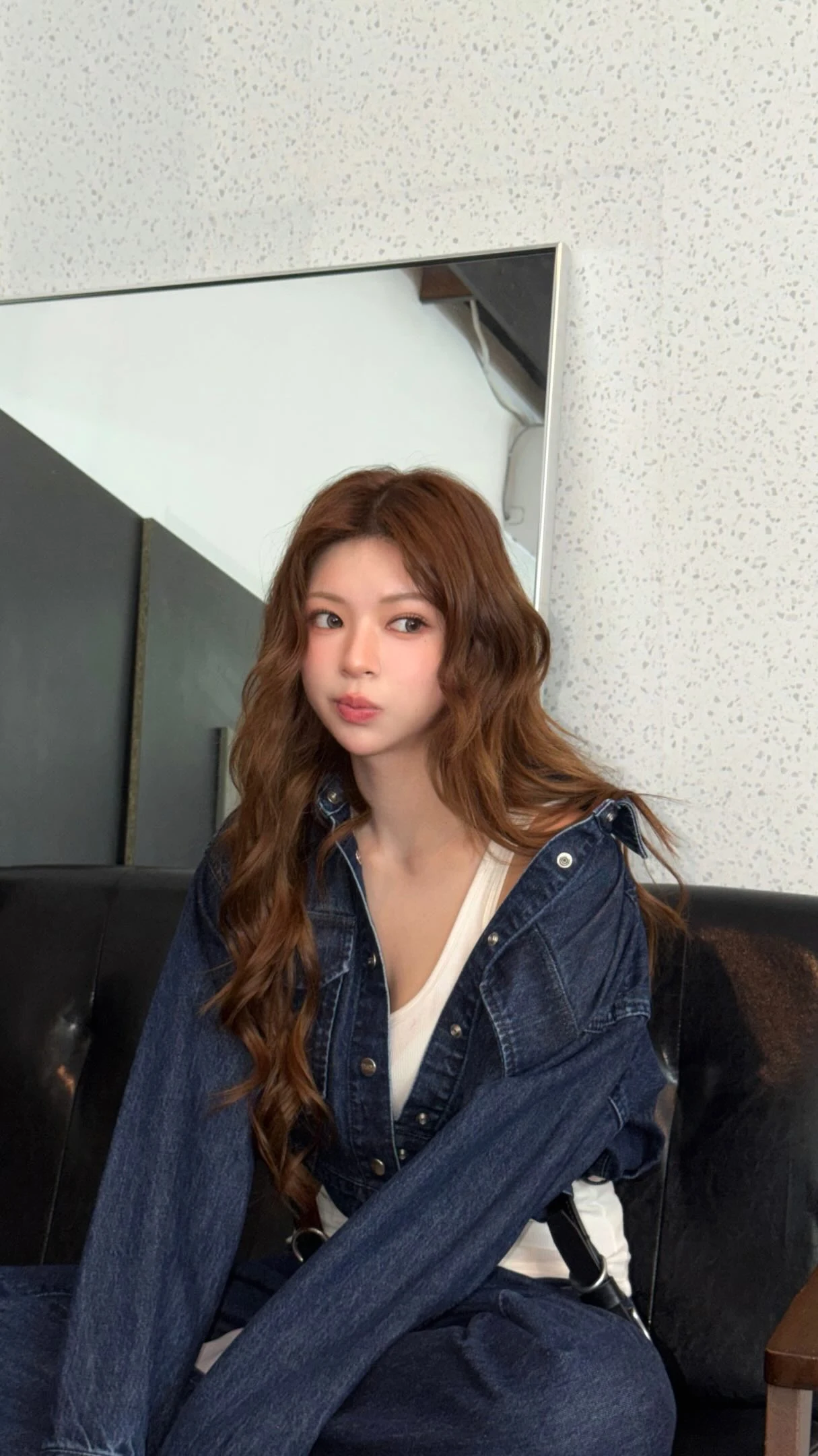 Oversized dark denim jacket draped off shoulders over a white V-neck top and dark denim bottoms.
