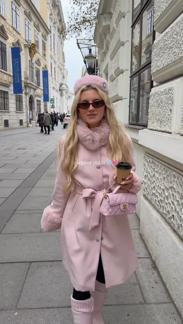 Woman in a belted pastel pink wool coat, pink beret, tall pink boots, and quilted bag.