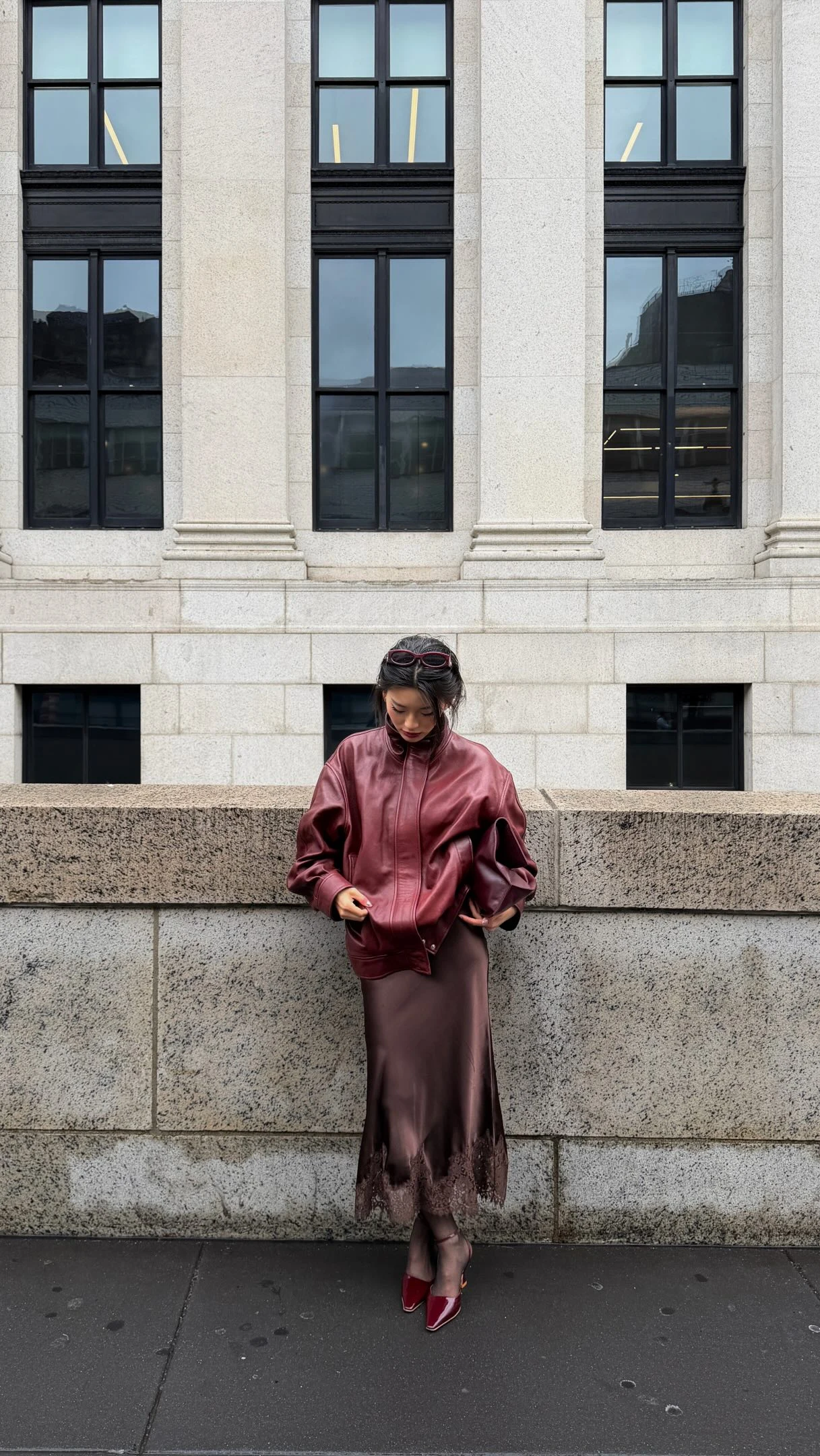 Woman wearing a plum leather bomber jacket, plum satin midi skirt, and black tights.