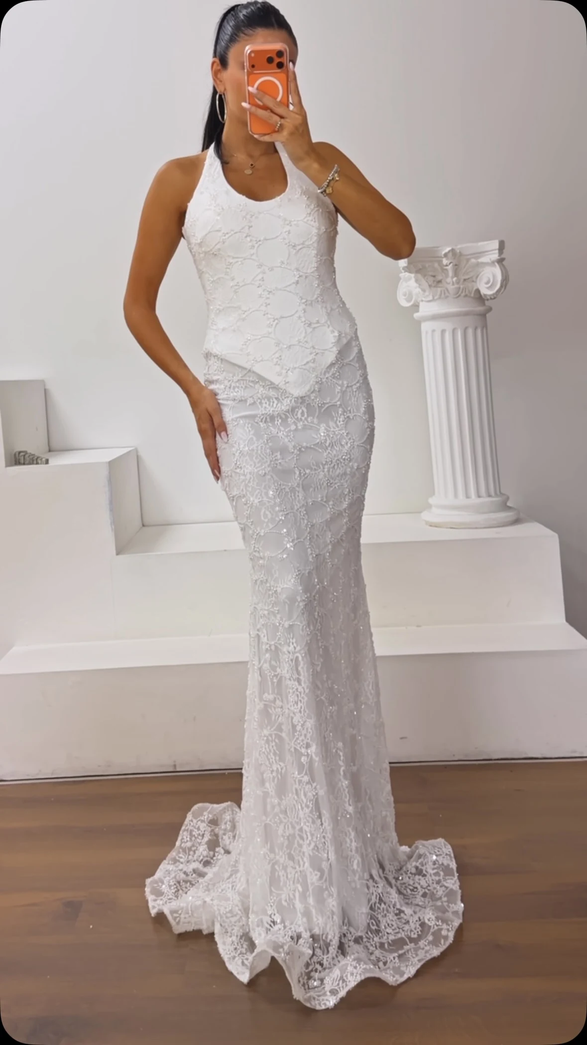 Woman wearing a white lace halter mermaid maxi dress with a slight trailing hem.