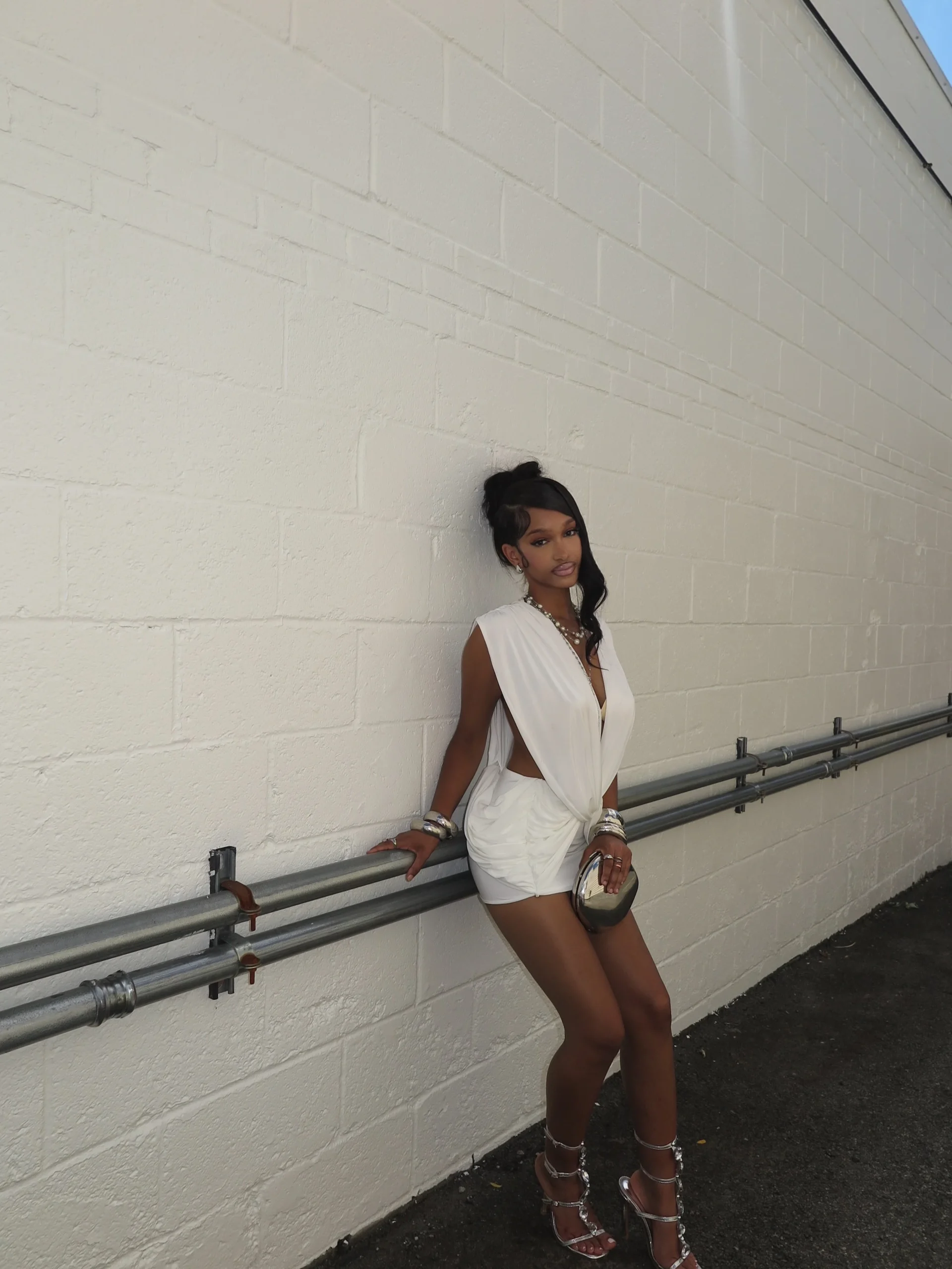 Woman wearing a white twisted-front mini dress with side cutout and silver strappy heels.