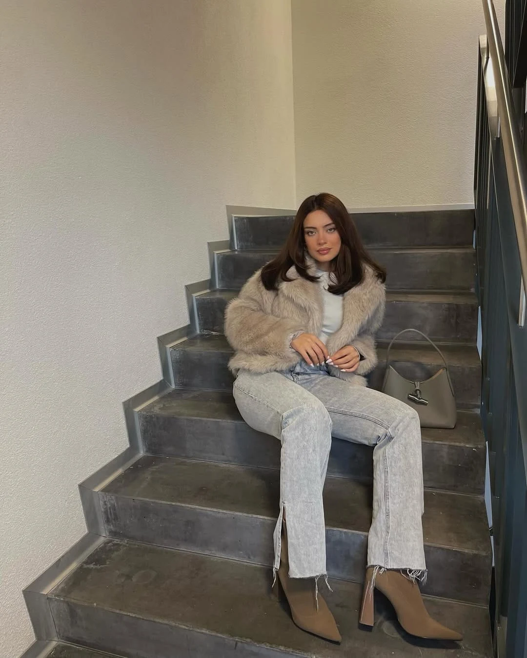 Woman wearing beige faux fur jacket, split-hem jeans, and tan pointed ankle boots with a taupe bag.