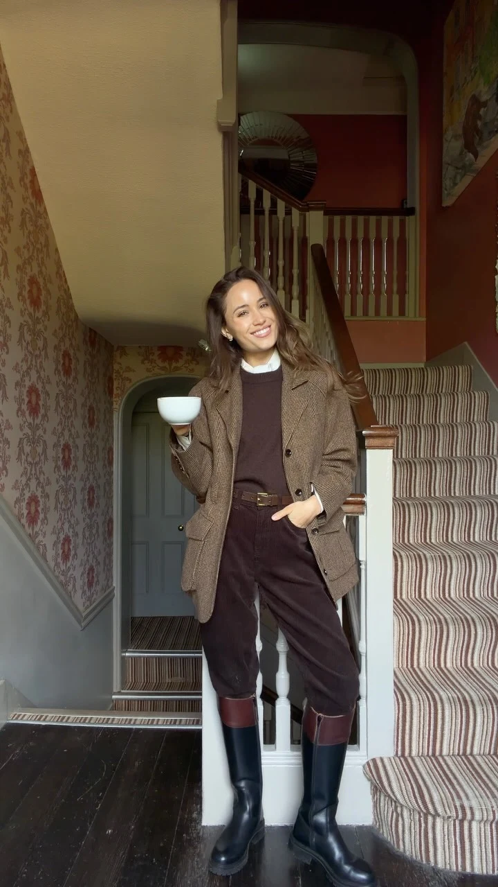 Brown checked blazer over dark sweater and white shirt with dark trousers tucked into tall boots.