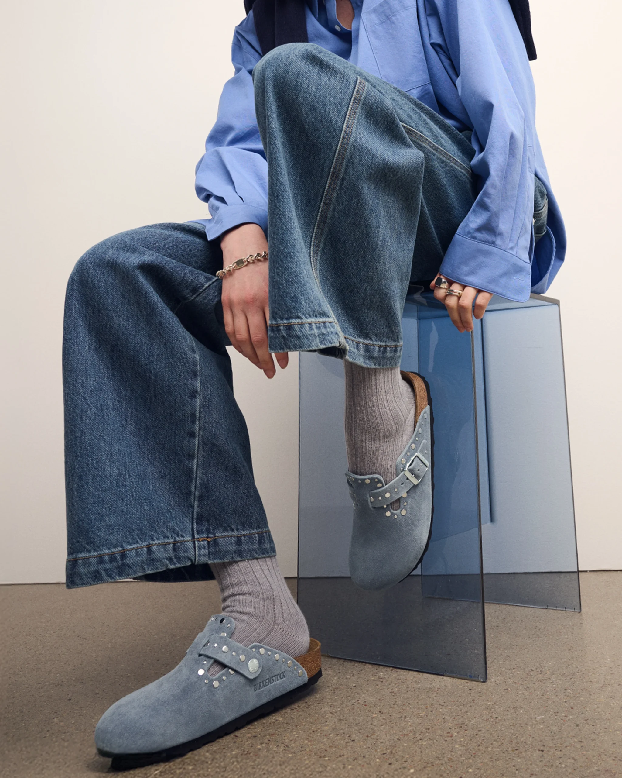Two outfit variations featuring wide-leg jeans, a denim skirt, and light blue-gray suede Boston clogs.