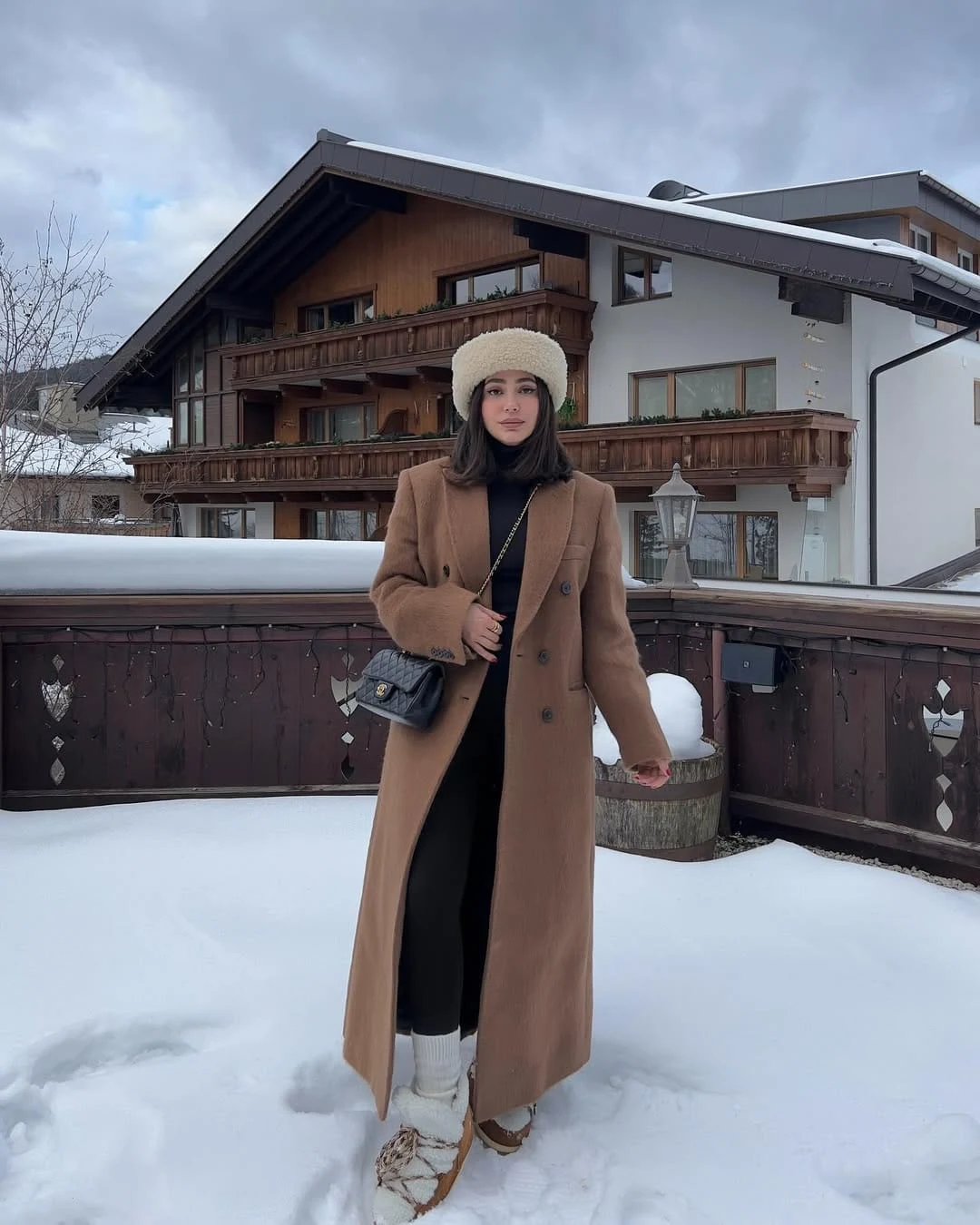 Camel long coat over black turtleneck and leggings, styled with a cream hat and chunky boots.
