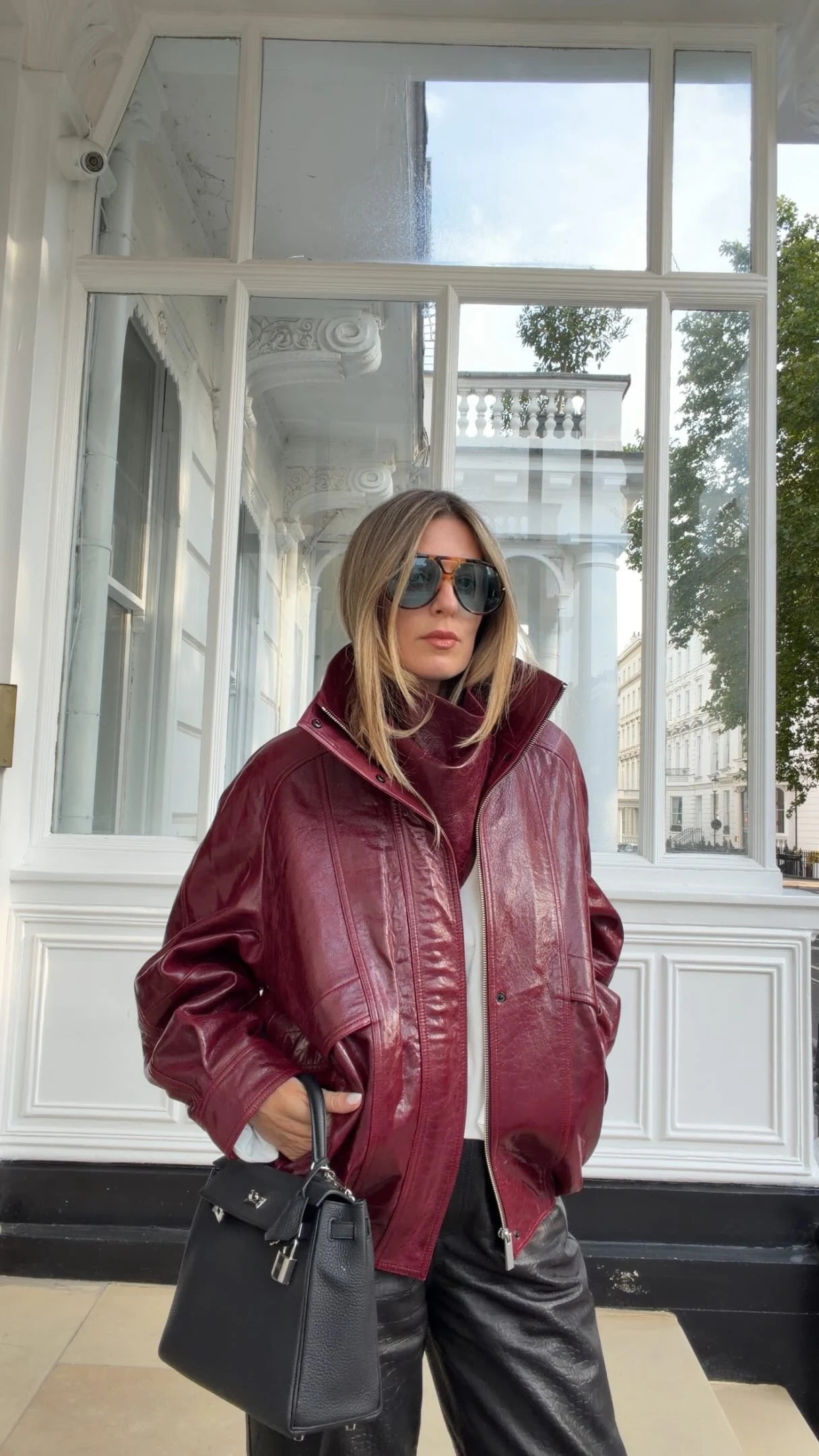 shiny cherry-red leather bomber jacket, white top, black croc-embossed leather trousers, black loafers, small black structured handbag
