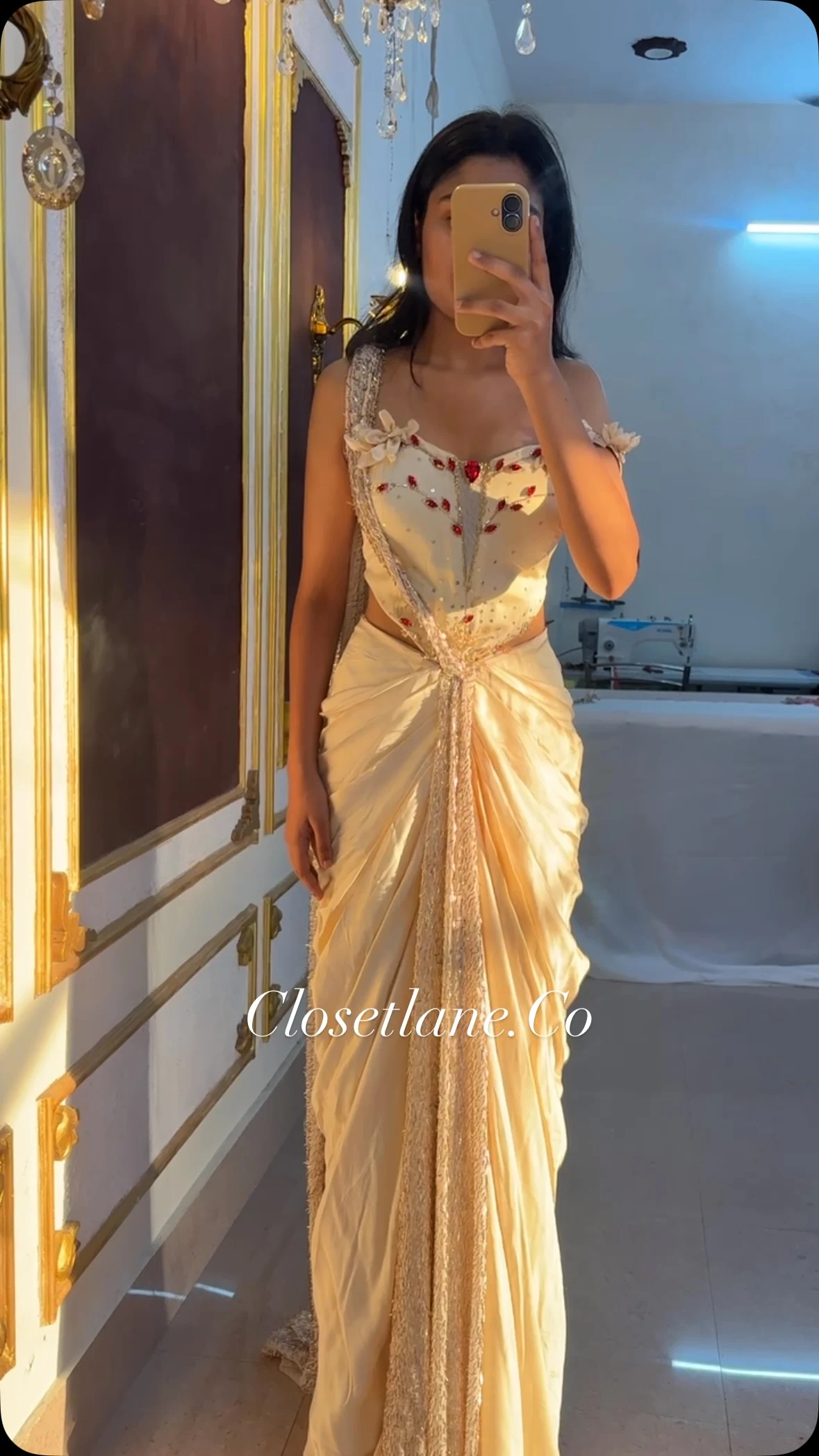Cream draped floor-length gown with a fitted corset bodice, off-shoulder sleeves, and a central jewel accent.