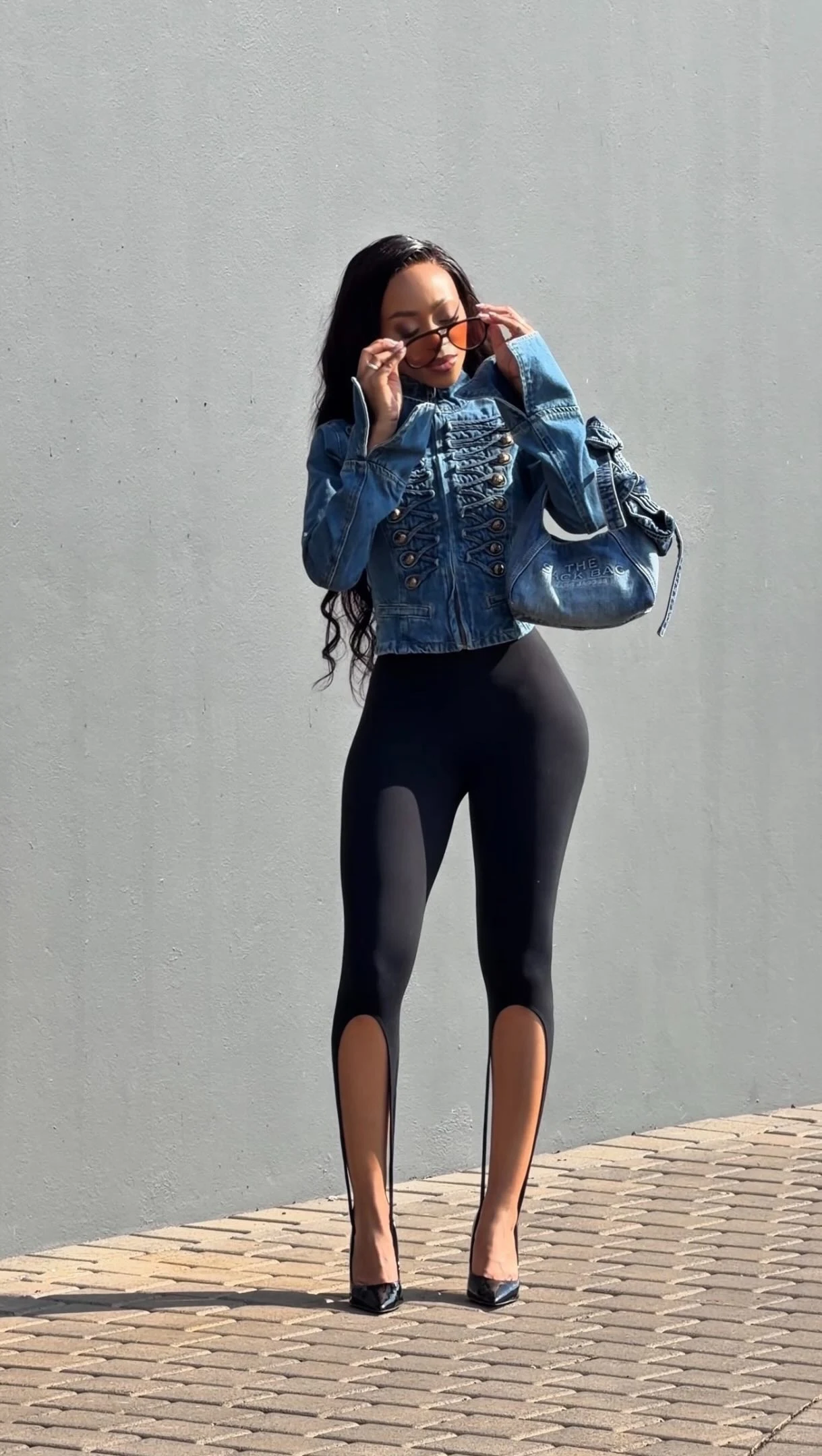 Cropped blue denim jacket with lacing paired with cutout black leggings, pointed heels, and a blue bag.
