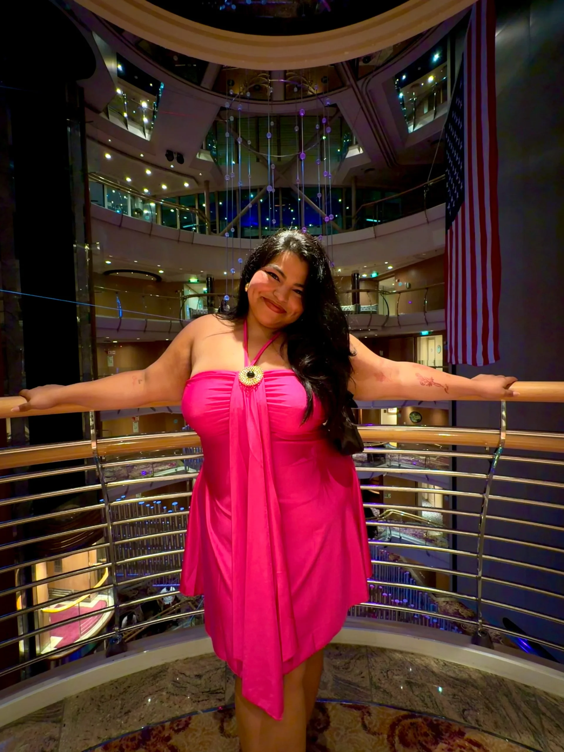 Woman in a bright fuchsia halter mini dress with a circular brooch at the neckline.