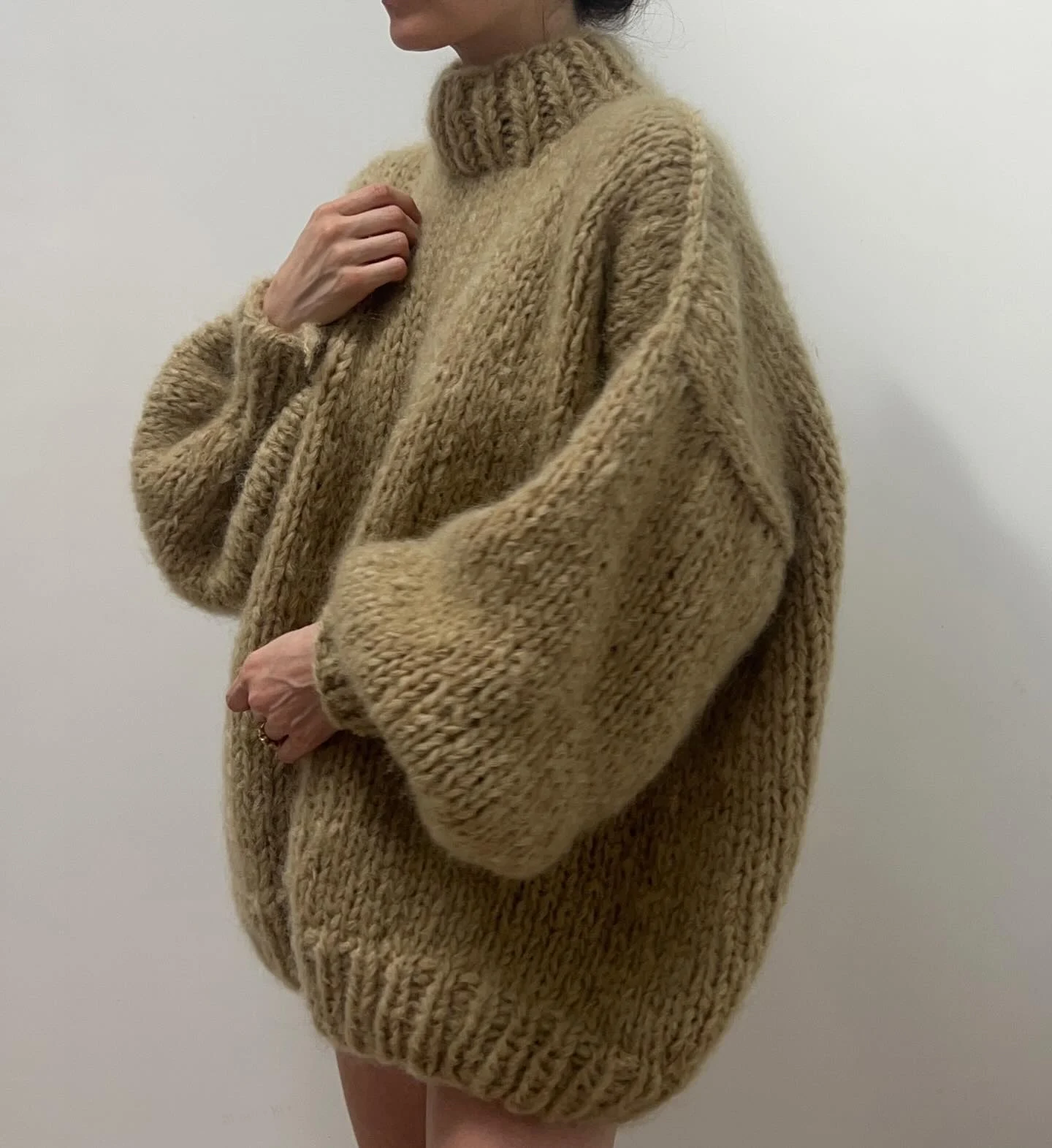 Oversized beige chunky turtleneck sweater with voluminous sleeves against a light wall.