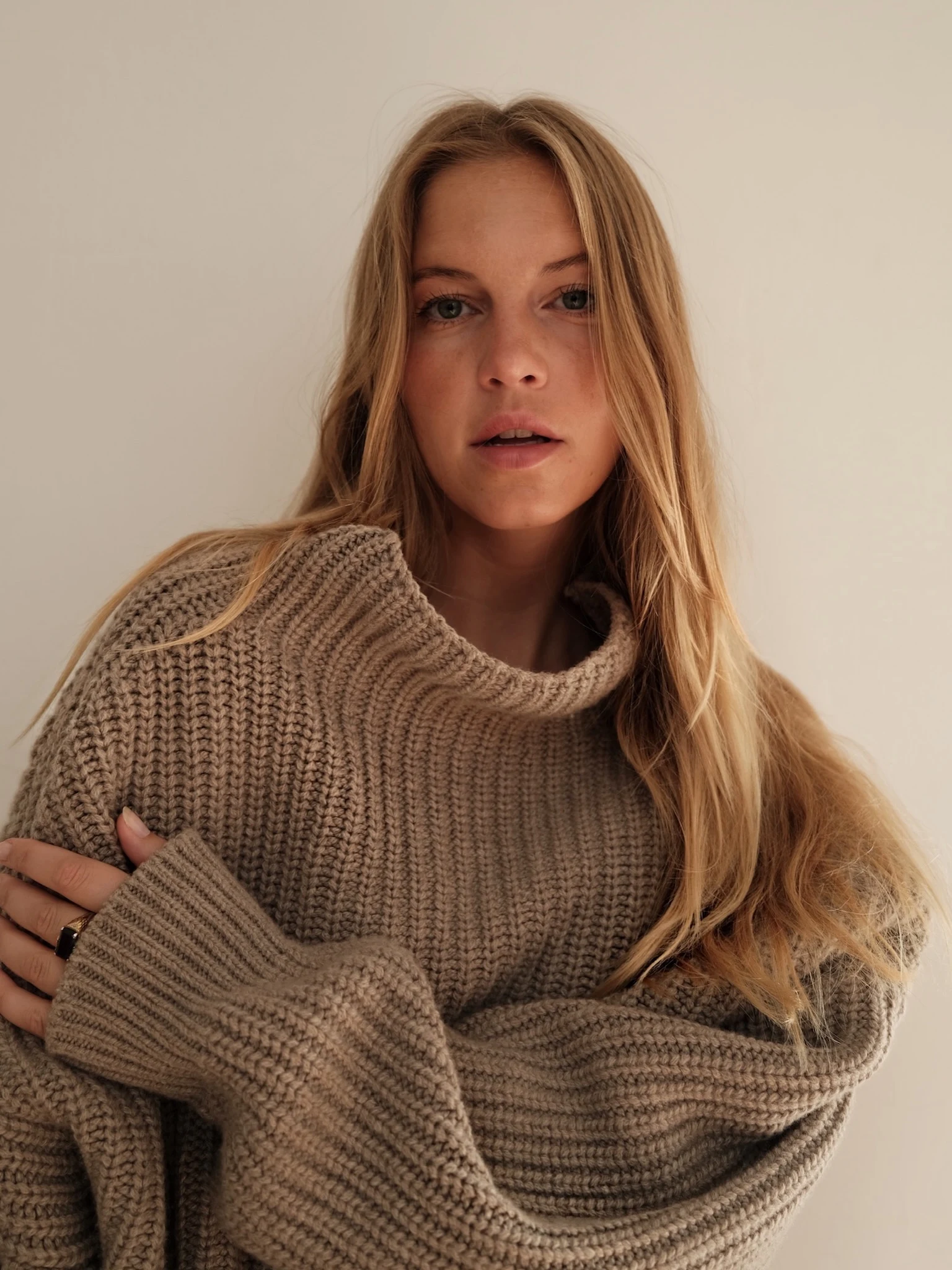 Person wearing a chunky oversized taupe ribbed turtleneck sweater with sleeves covering the hands.
