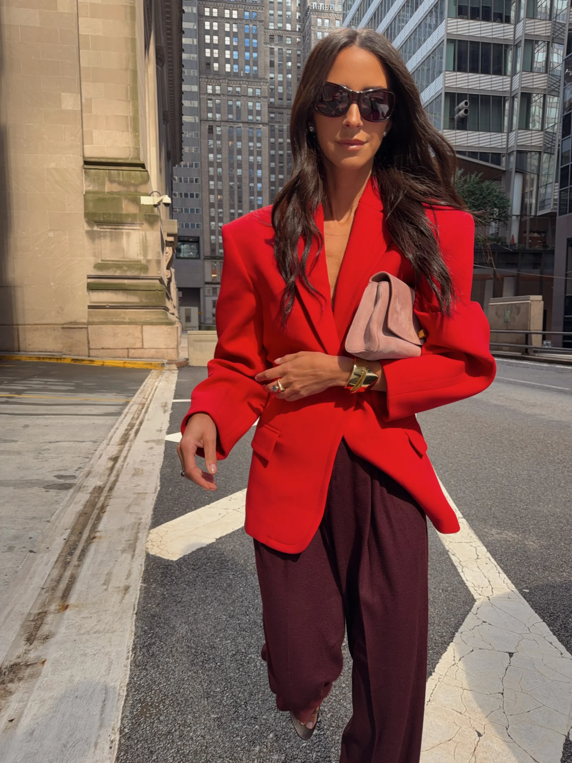 Person in a red blazer and burgundy wide-leg trousers with a pink clutch on a city street.