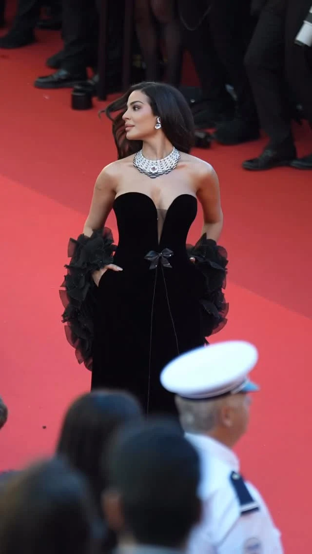 A person in a black strapless sweetheart gown with layered ruffled sleeves and a silver statement necklace.