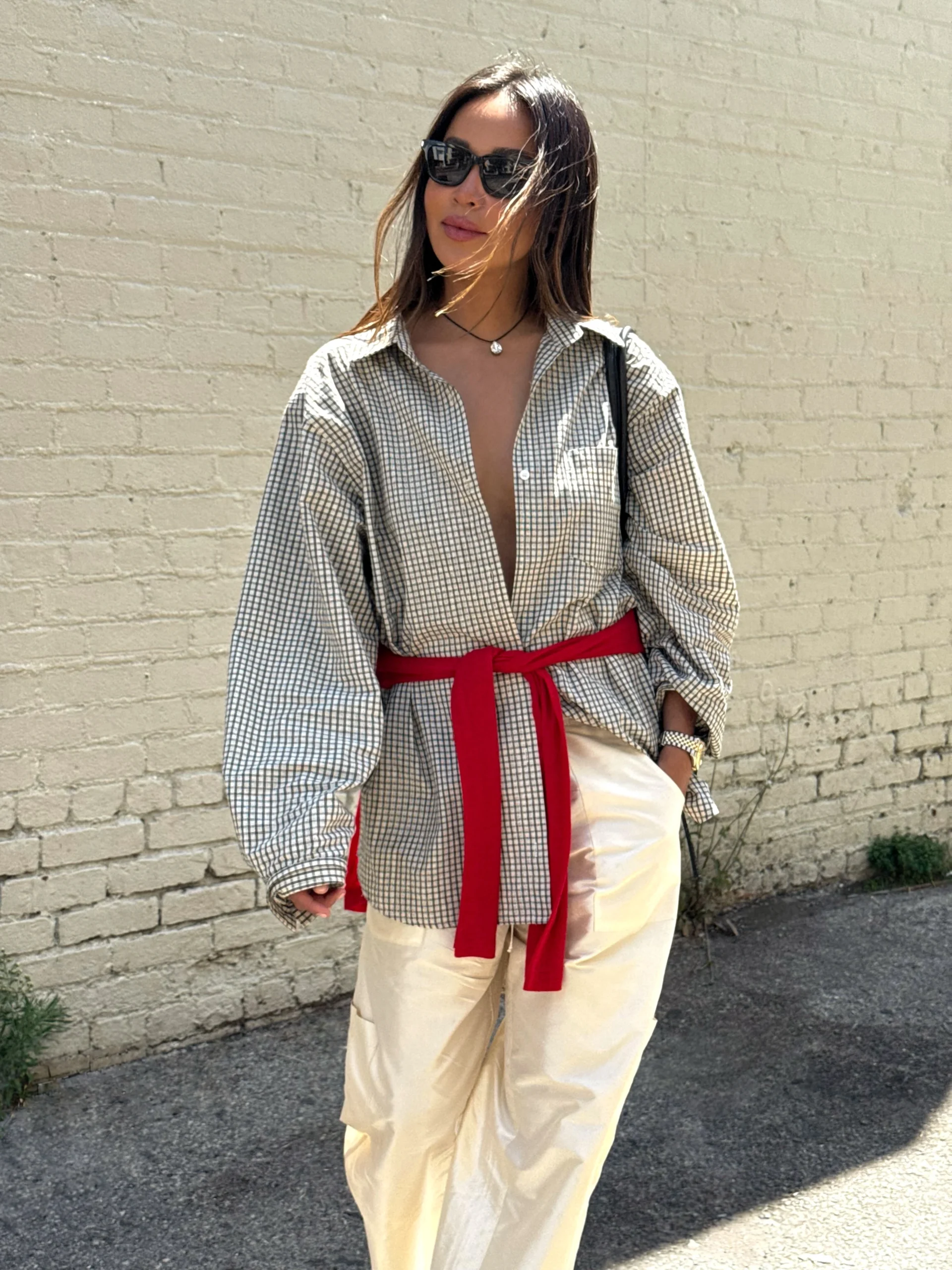 Oversized black-and-cream checked shirt with a wide red sash tied at the waist over cream trousers.
