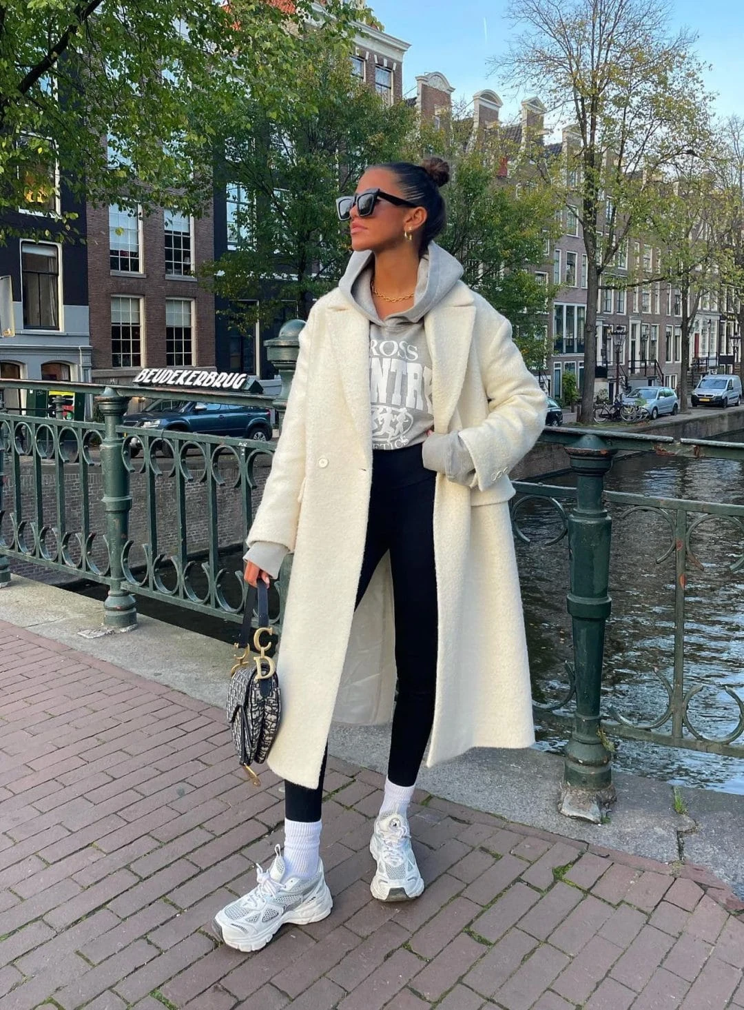 A grey hoodie layered under a long white wool coat creates the ultimate chic yet cozy outfit. Paired with black leggings, chunky white sneakers, gold jewelry, and a designer handbag, this look is perfect for running errands while staying stylish.