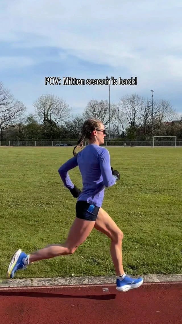 Runner in a lavender long-sleeve top, black shorts, and blue shoes on an outdoor track.