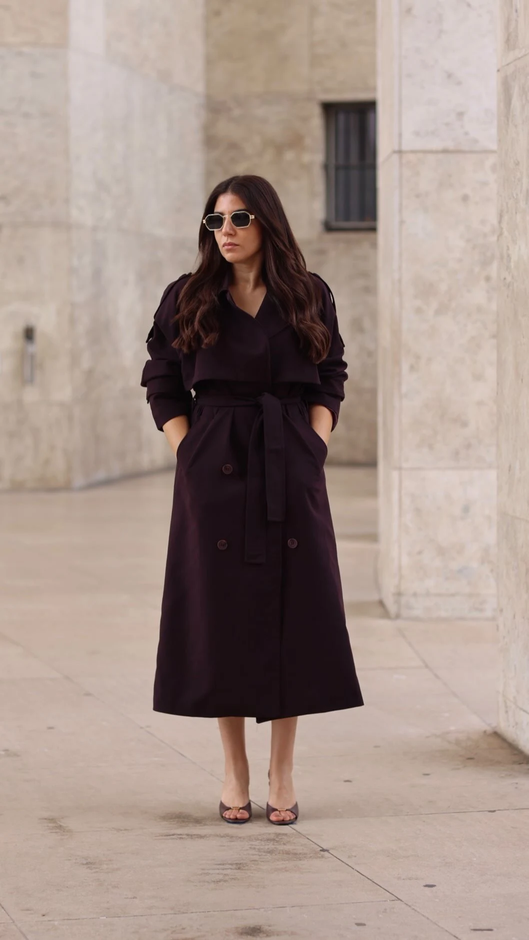 Woman in a long plum double-breasted trench coat, black top, and dark wide-leg trousers.