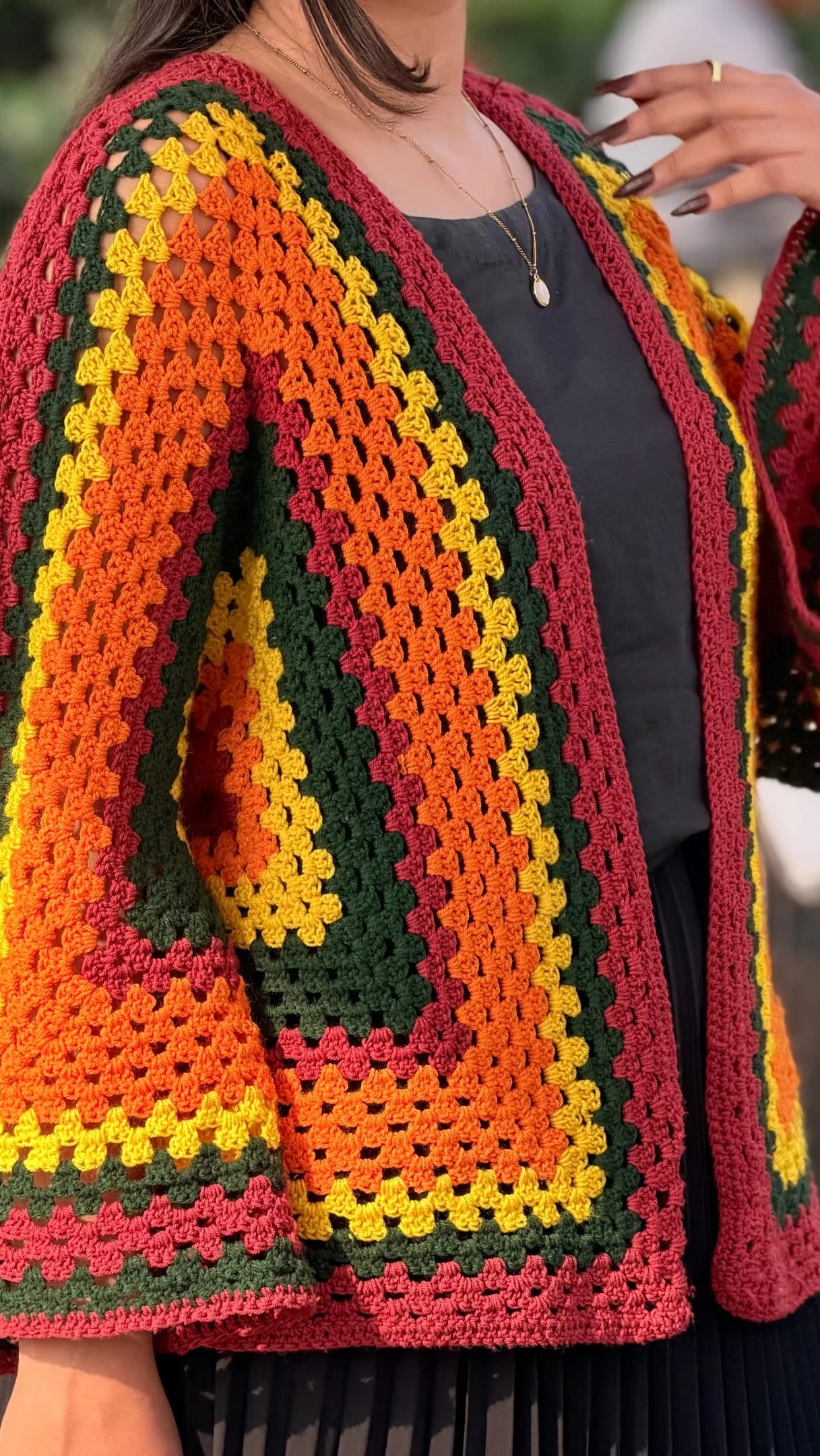 Colorful open crochet cardigan with orange and green bands over a dark charcoal top and skirt.