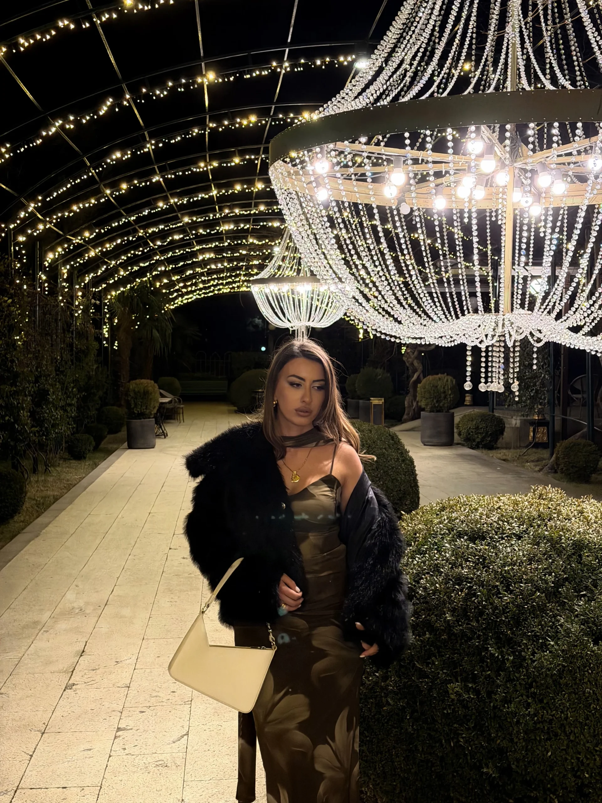 Fitted olive floral slip dress with a voluminous black fur jacket draped over the shoulders outdoors.