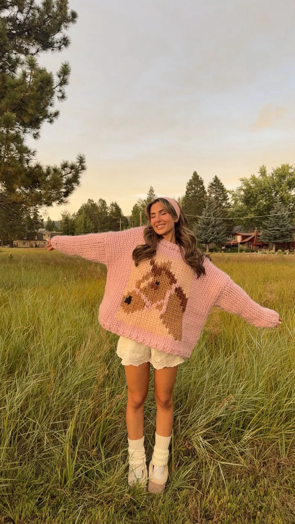 Chunky pink sweater with animal motif worn over white scalloped shorts with white crew socks.