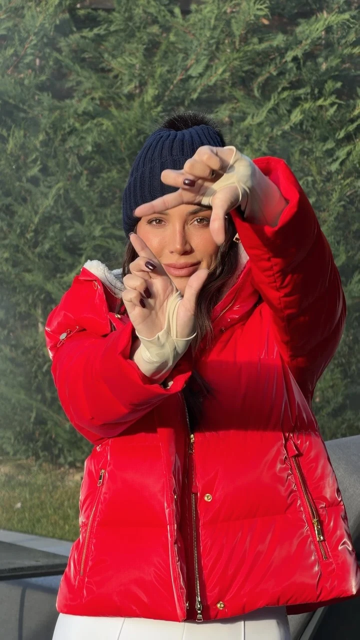 Woman in a bright red puffer jacket, white wide-leg pants, and a dark blue knit beanie.