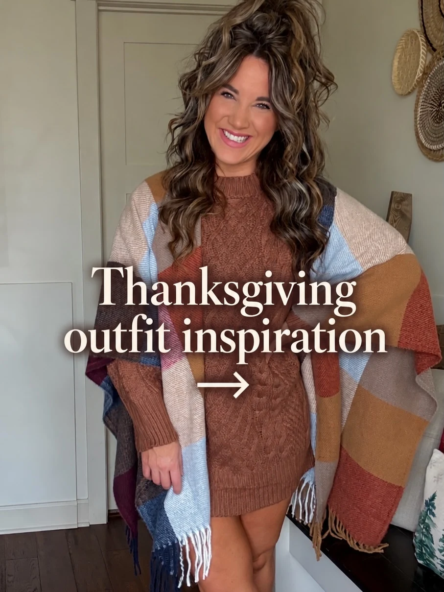 Person in a rust-brown cable-knit sweater dress draped with a large multicolor fringed shawl.